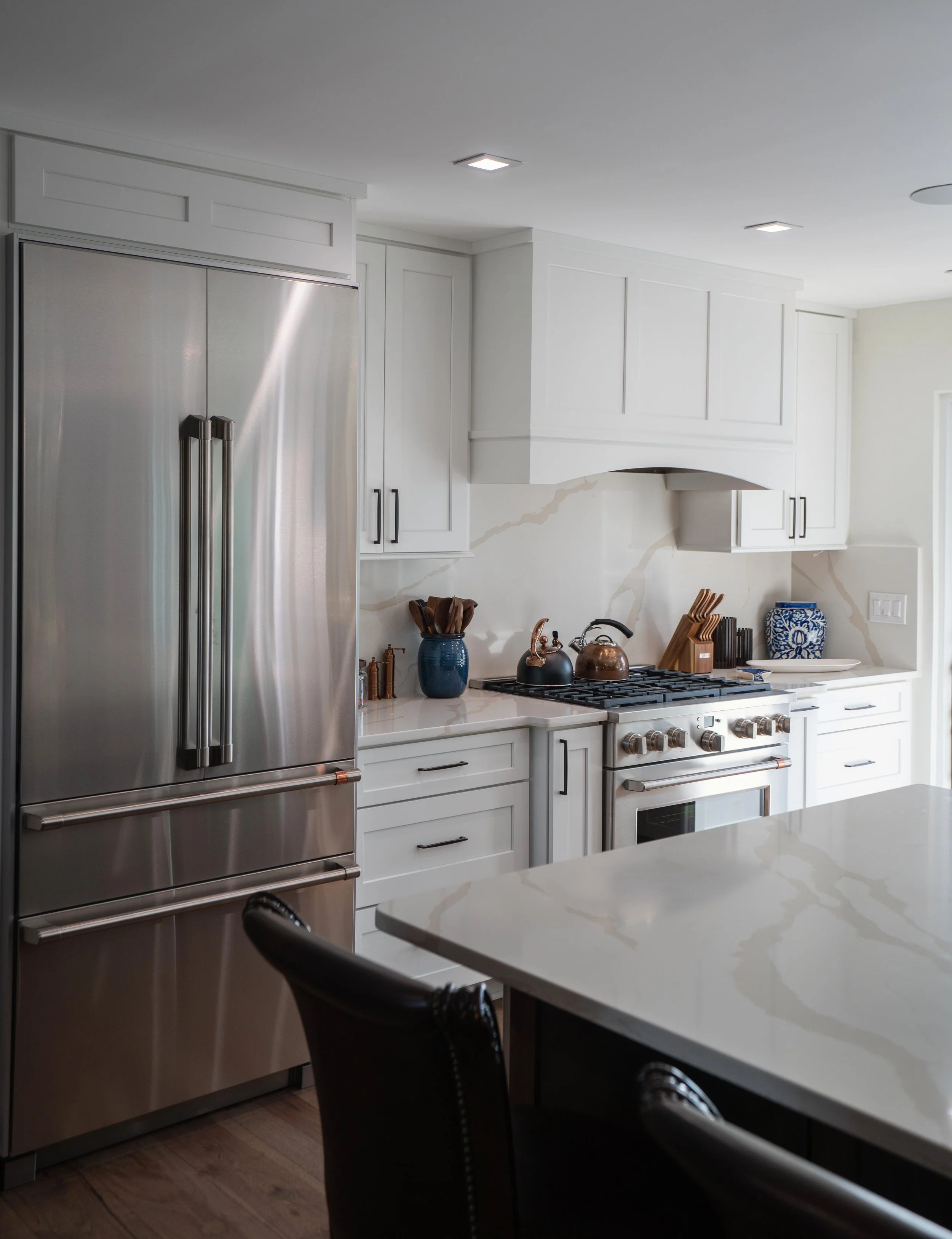 Modern kitchen with white cabinets, stainless steel refrigerator, and marble backsplash, featuring a kitchen island in the foreground.