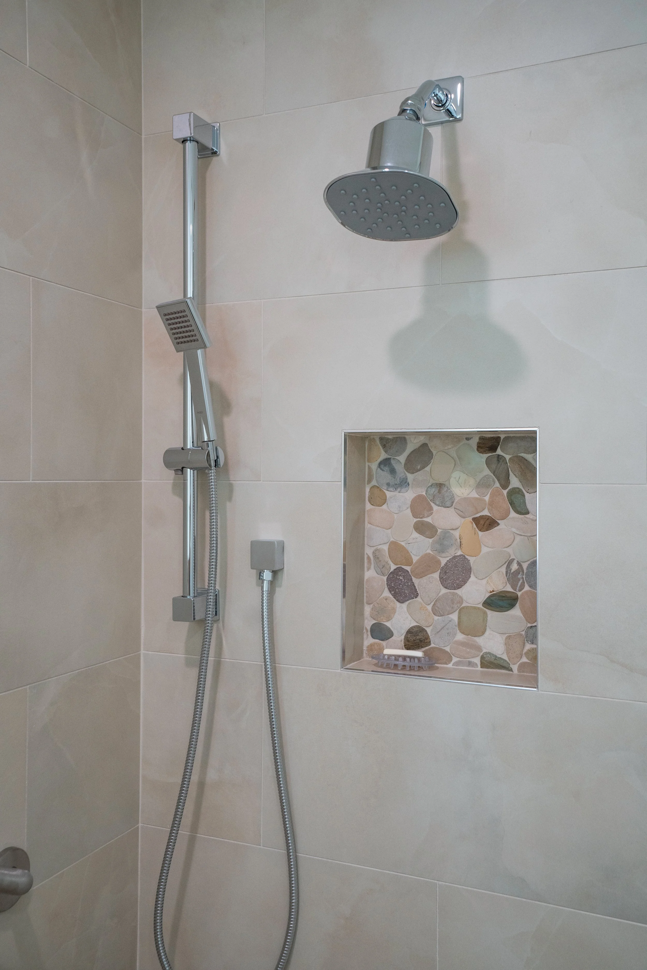 Showerhead, handheld shower, and niche with decorative stones in a bathroom shower.