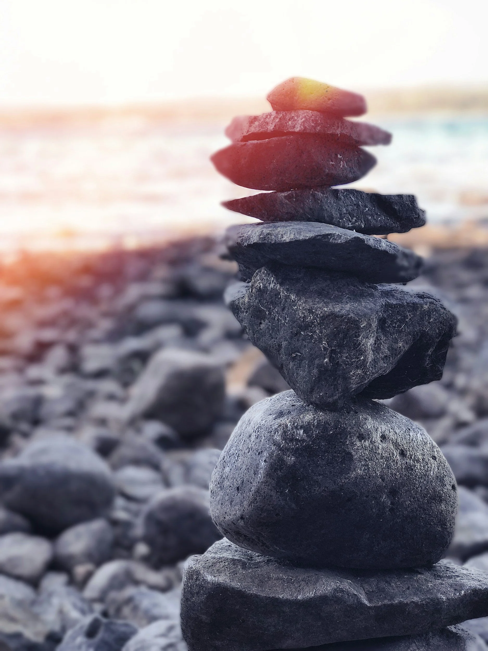 Stacked rocks on a rocky beach with blurred rocks in the background and sunlight