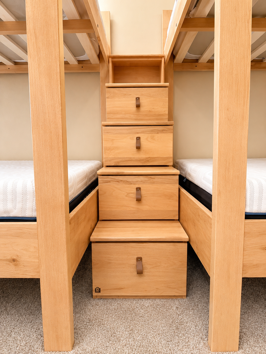 Wooden bunk beds with a staircase and built-in drawers in the middle, with mattresses on either side.