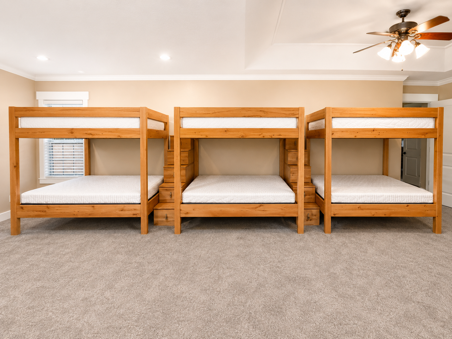 Three wooden bunk beds in a brightly lit room with beige walls, a ceiling fan, and a window with blinds.