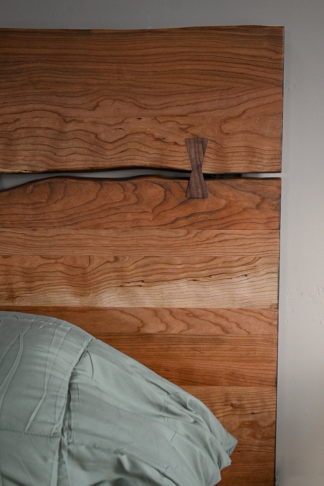 Close-up of a wooden headboard with a small wooden decorative piece and a pillow with a light-colored sheet.