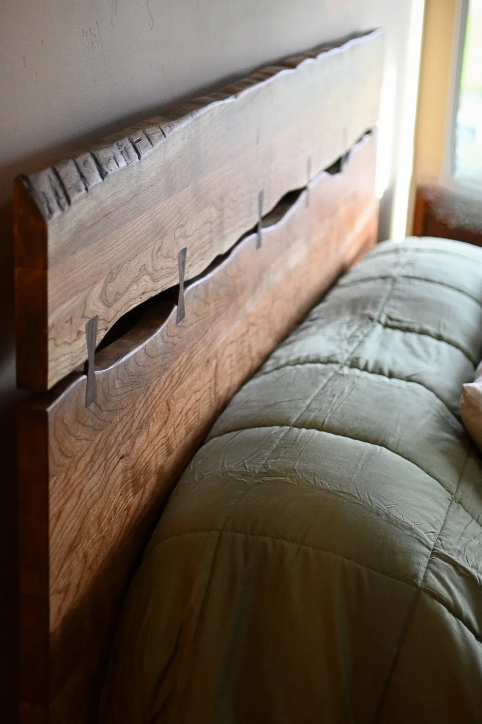 Close-up of a wooden bed headboard with built-in hooks and a beige quilted blanket on a bed.
