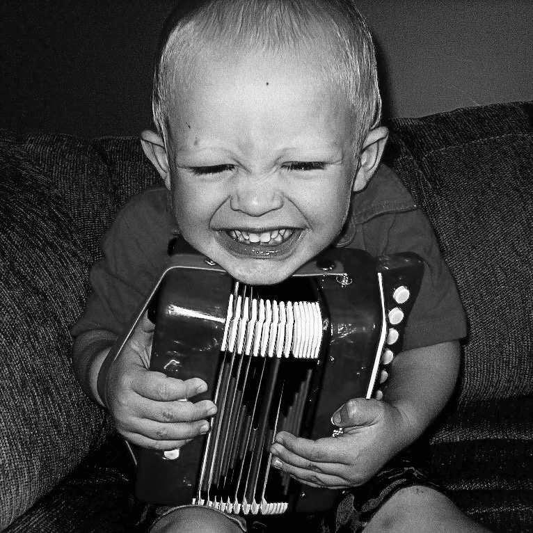 A young boy smiling while holding an accordion