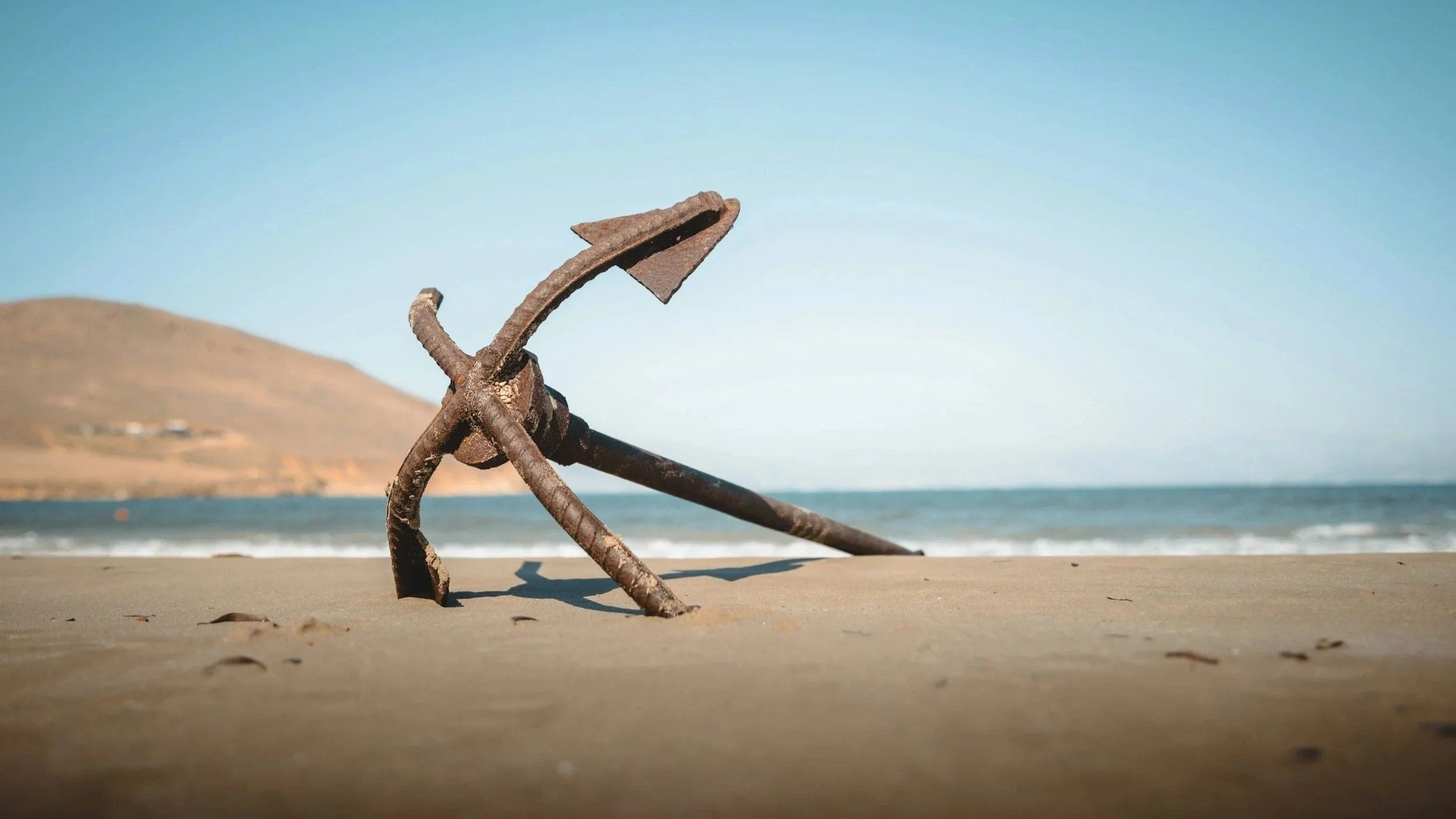 Old rusty anchor lying on sandy beach with ocean and distant hills in the background