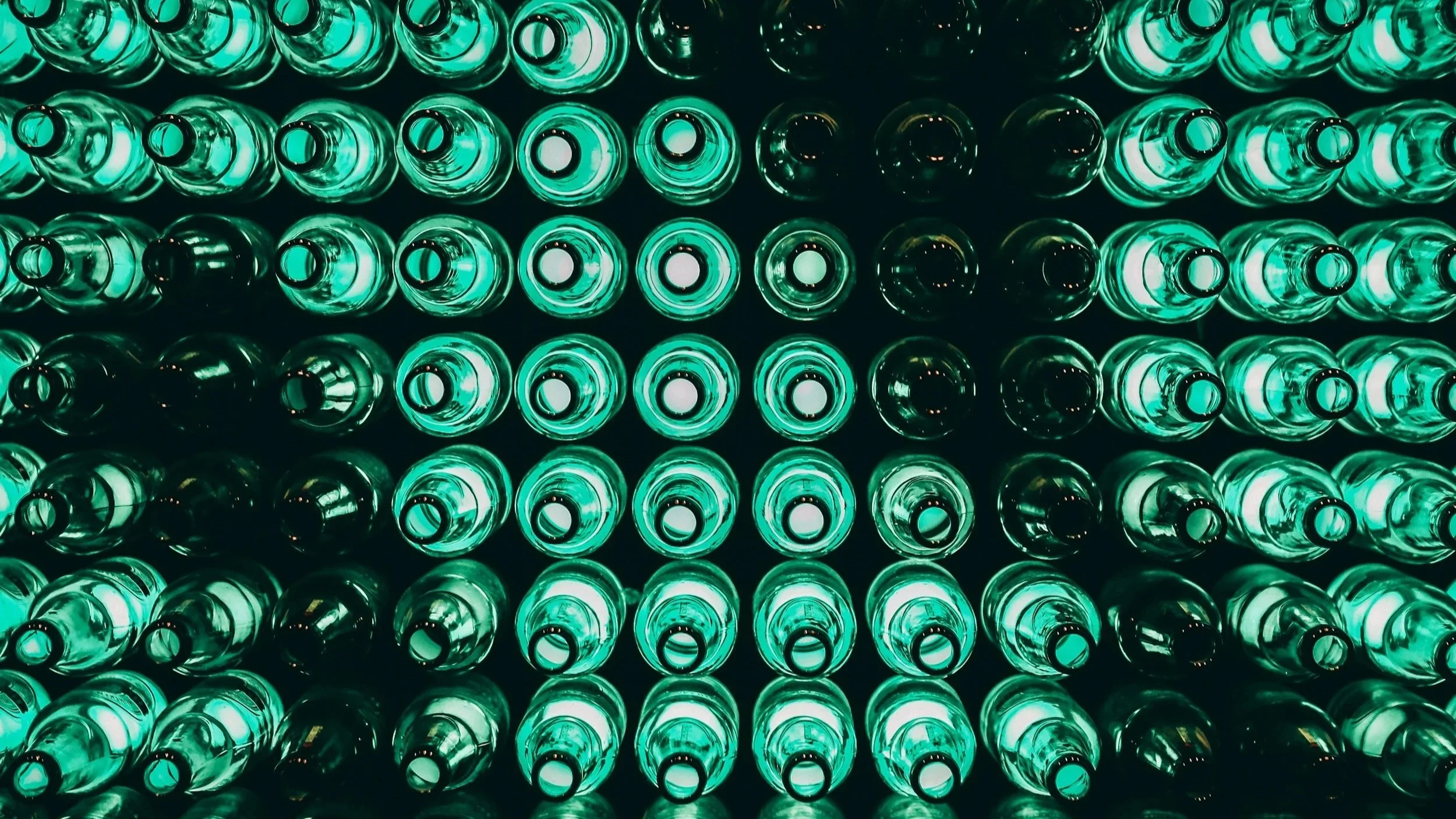 Multiple beer bottles viewed from the bottom, glowing with green lighting, arranged in a grid pattern.