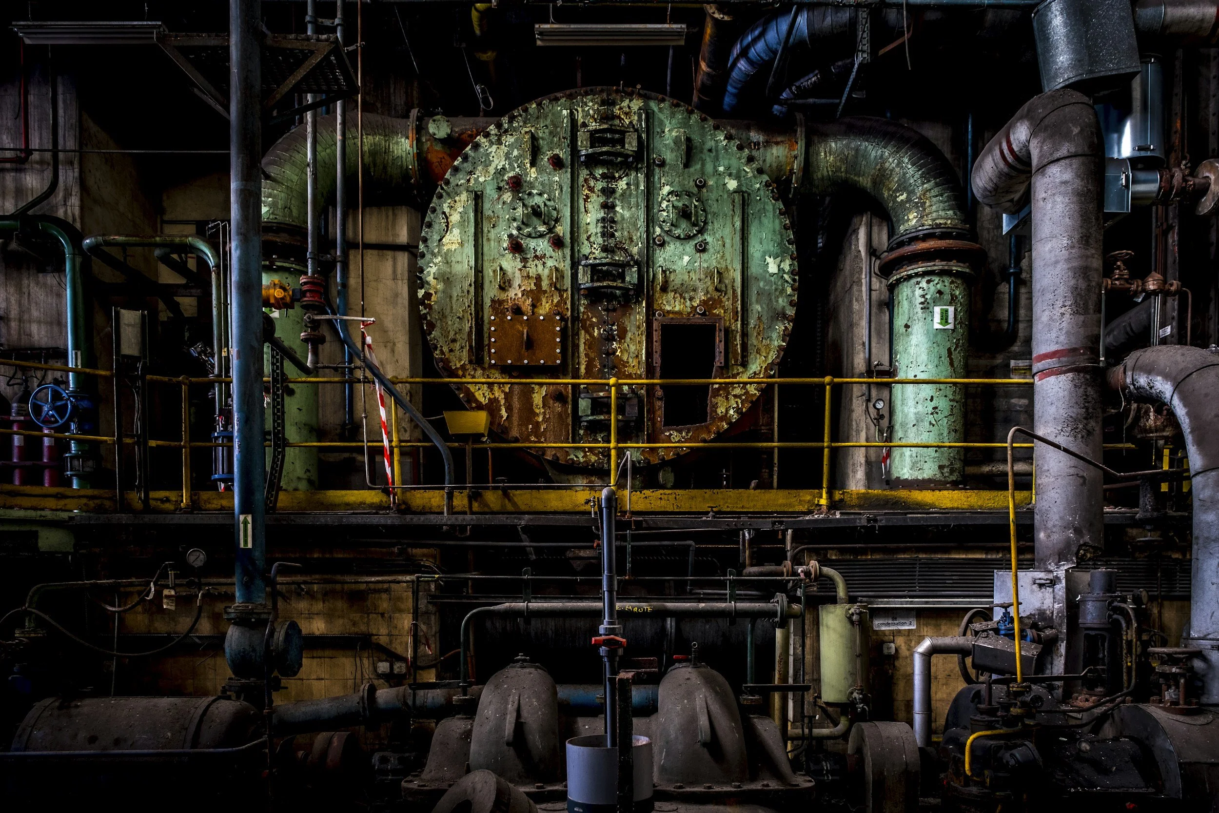 Old, rusted industrial machinery inside a factory, with large pipes and control valves.