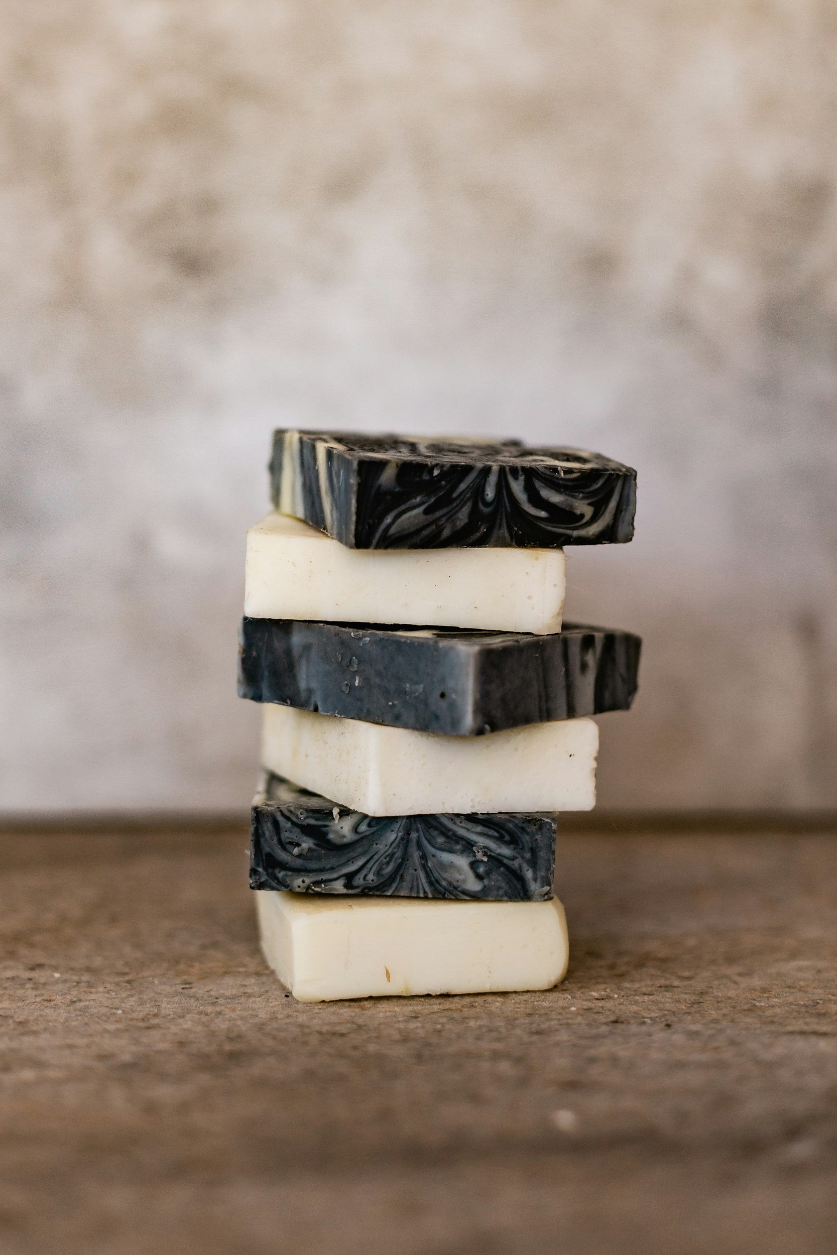 Stack of alternating black and white soap bars with marbled designs on a wooden surface, gray textured background.