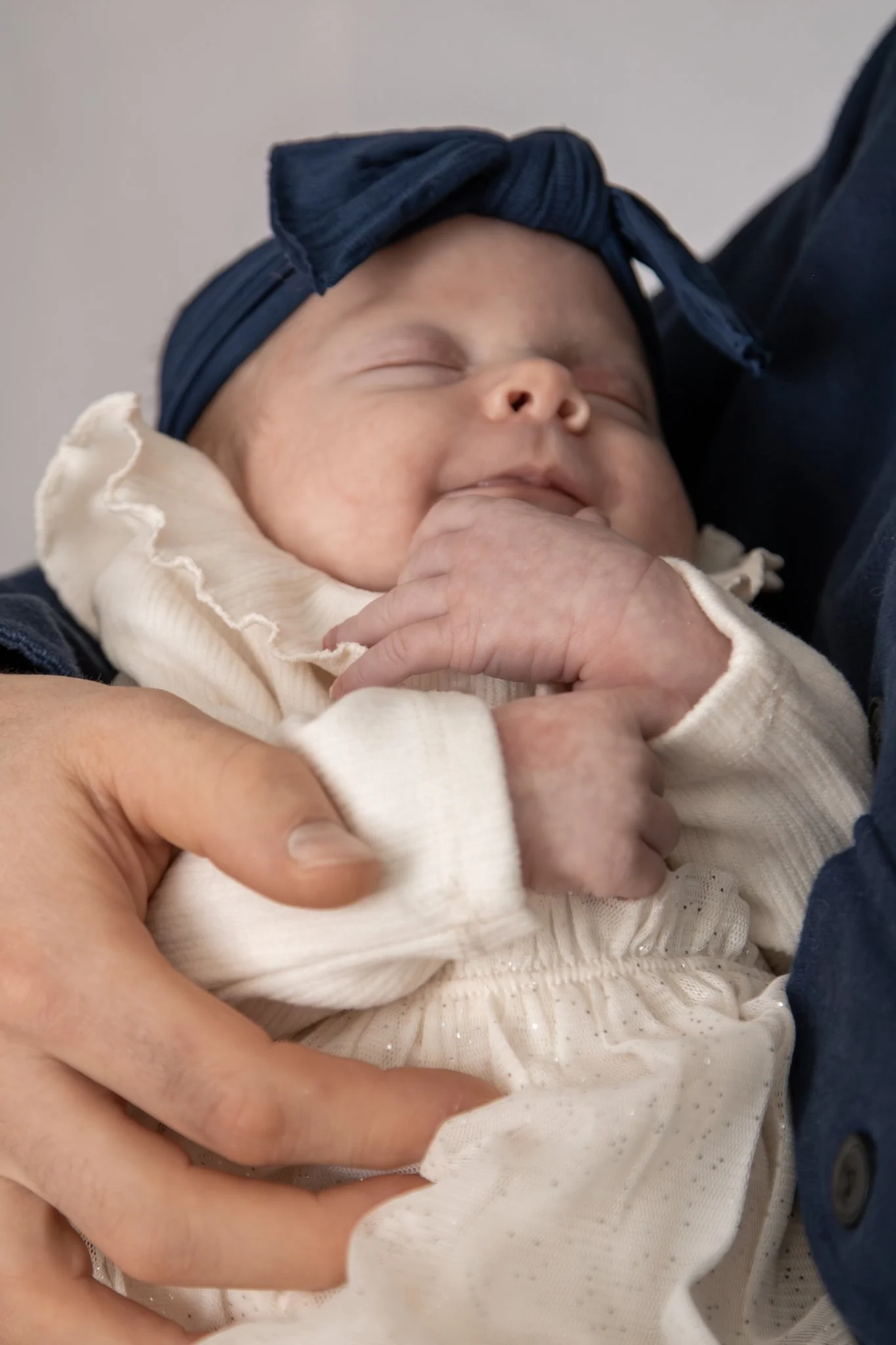 Close-up of a sleeping baby with a headband, resting in someone's arms.