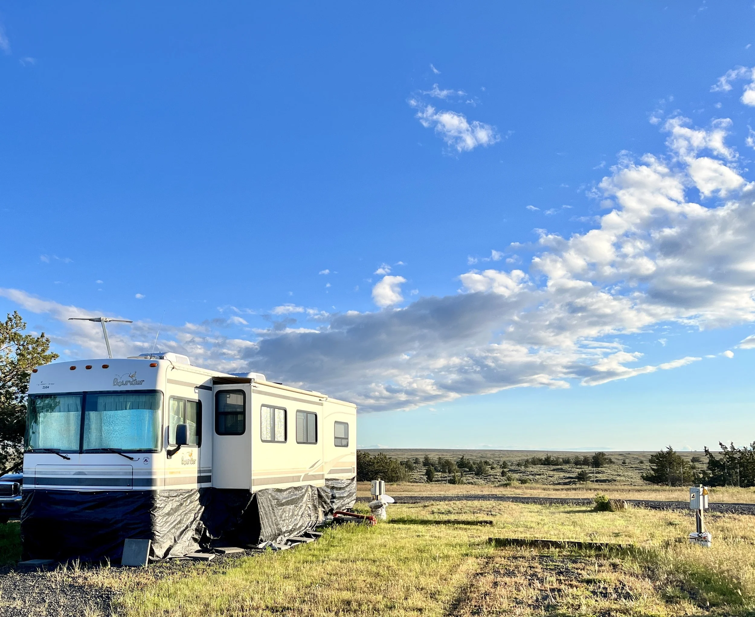 A white RV parked in an open field with a vast blue sky and scattered clouds overhead.