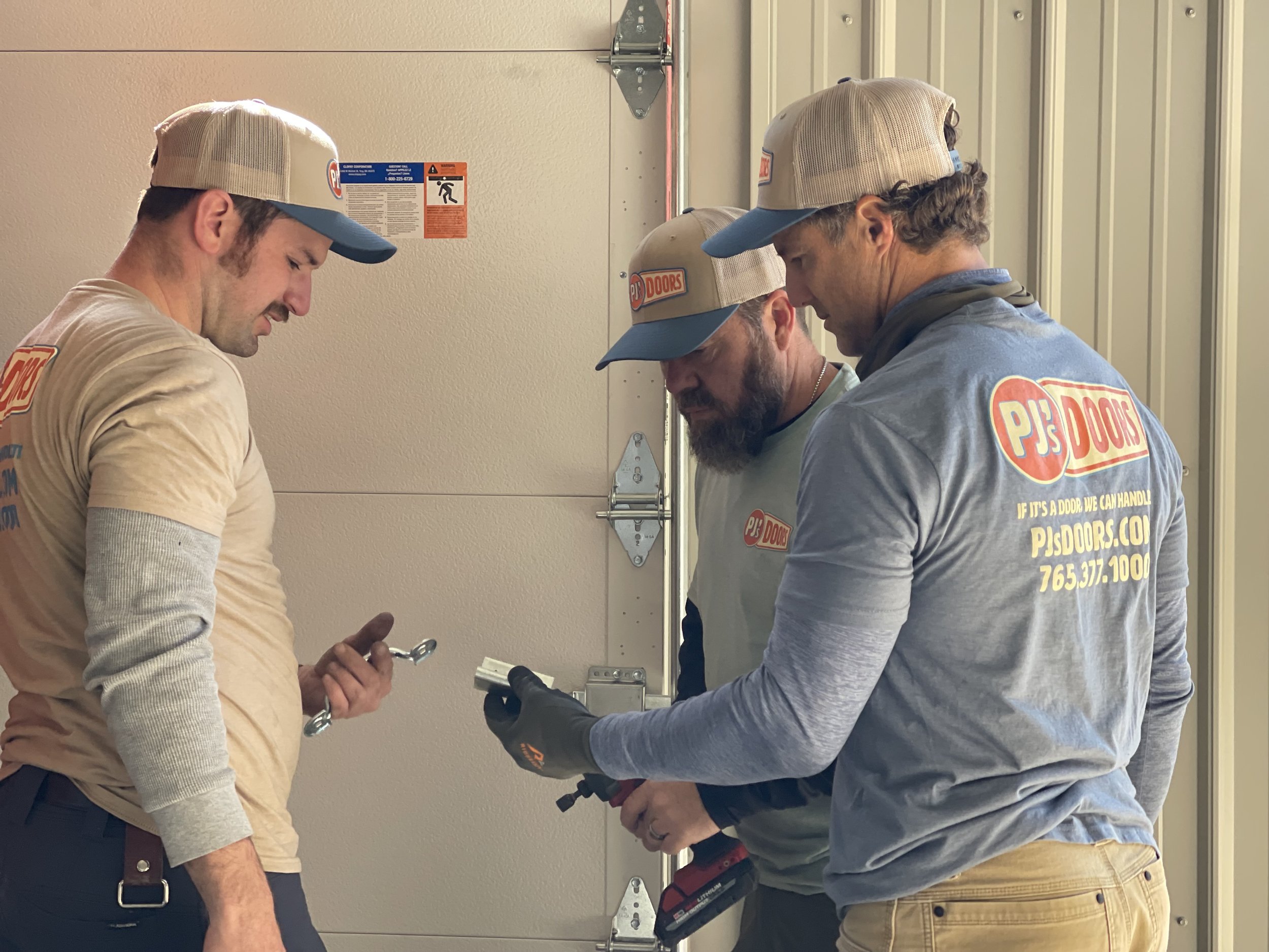 A man working on installing a white garage door in a garage construction site, with an open garage space and wooden framing inside.