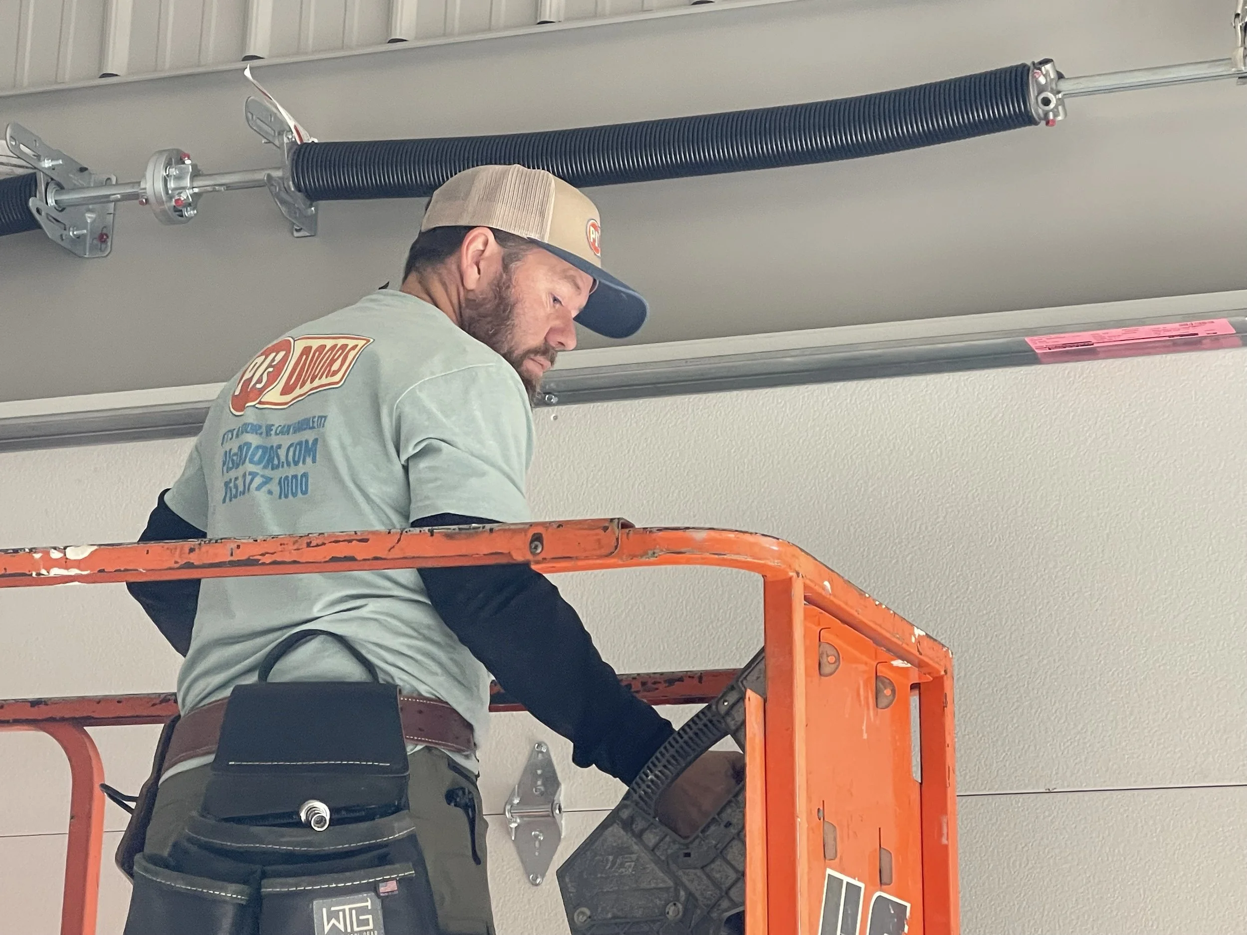 A man working on installing a white garage door in a garage construction site, with an open garage space and wooden framing inside.
