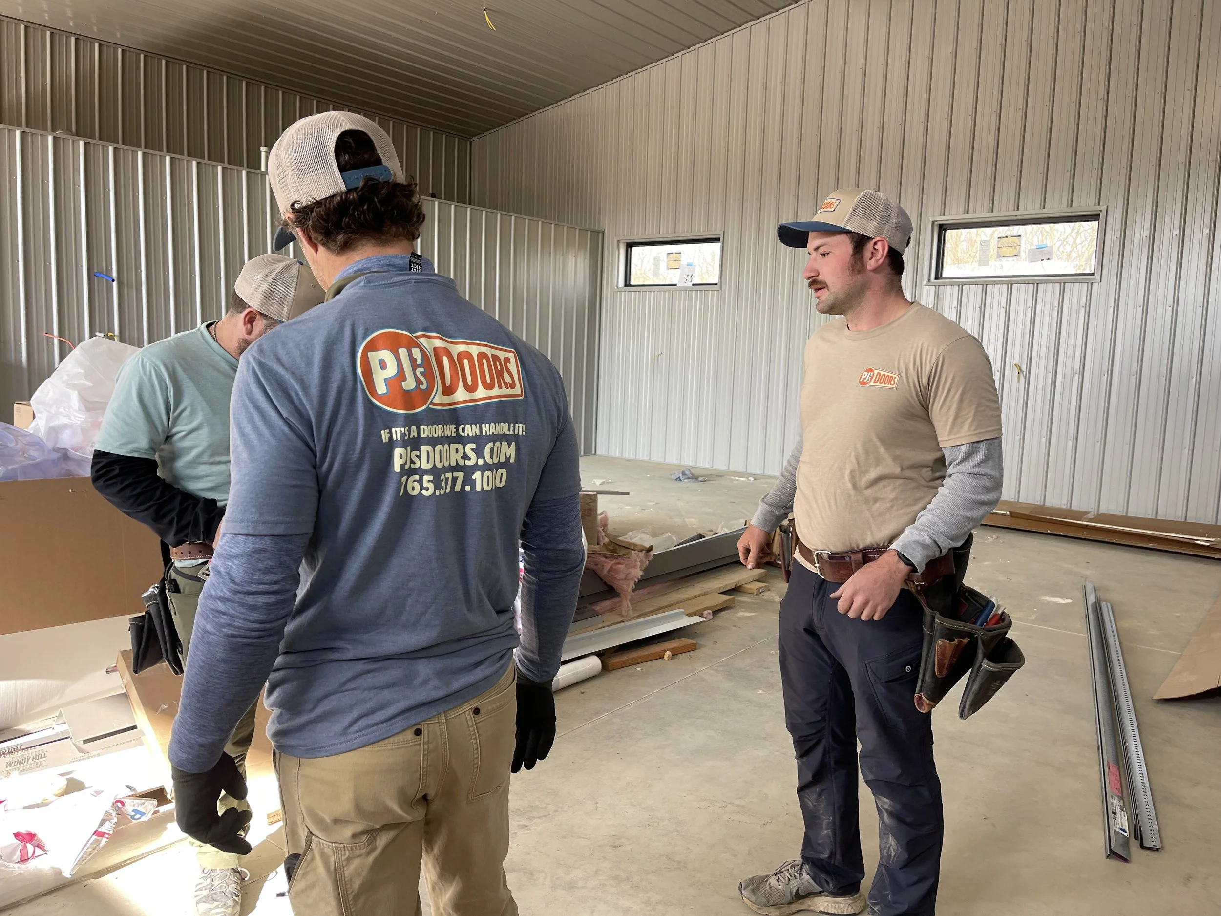 A man working on installing a white garage door in a garage construction site, with an open garage space and wooden framing inside.