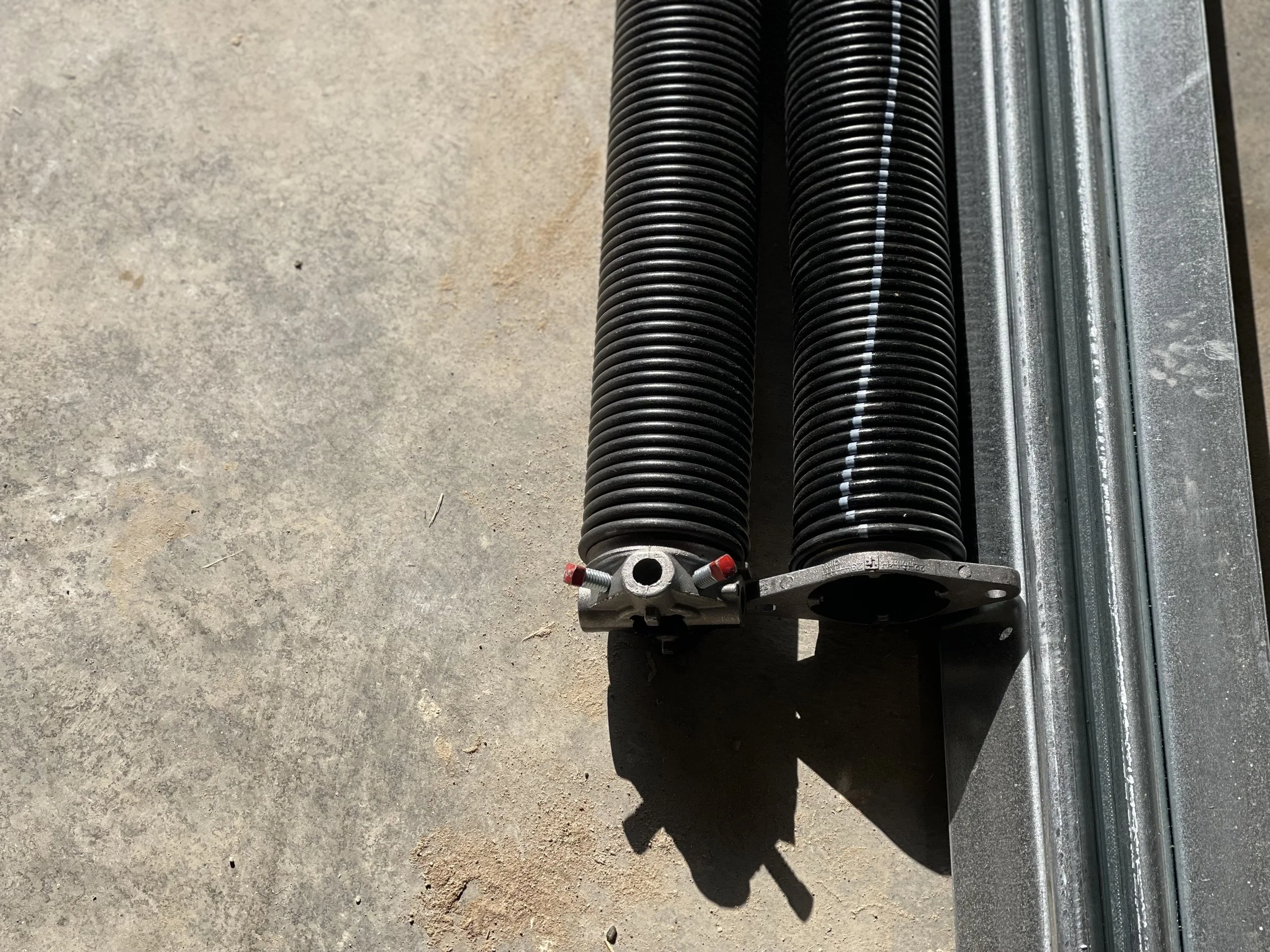 Two black flexible hoses connected to a metal fitting on a metal frame, placed on a concrete surface.