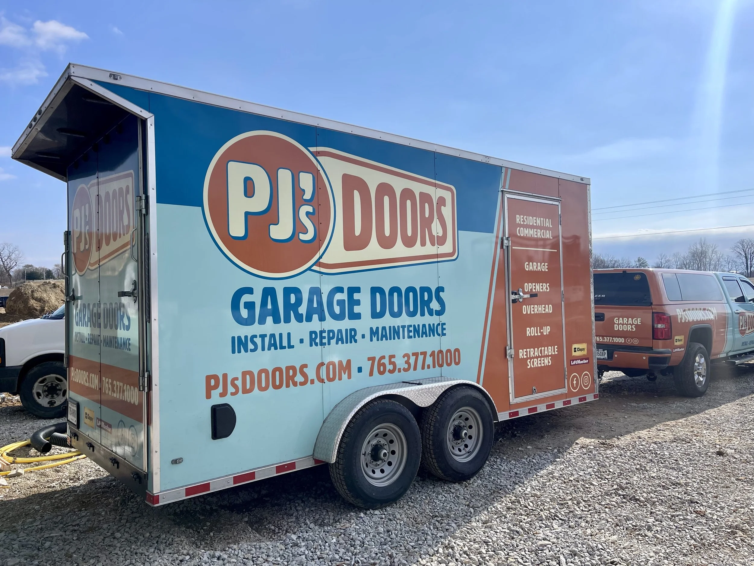 Two smiling men taking a selfie indoors, with a garage door in the background. One wears a black cap, and the other wears a gray cap with a 'New Horizons' logo.