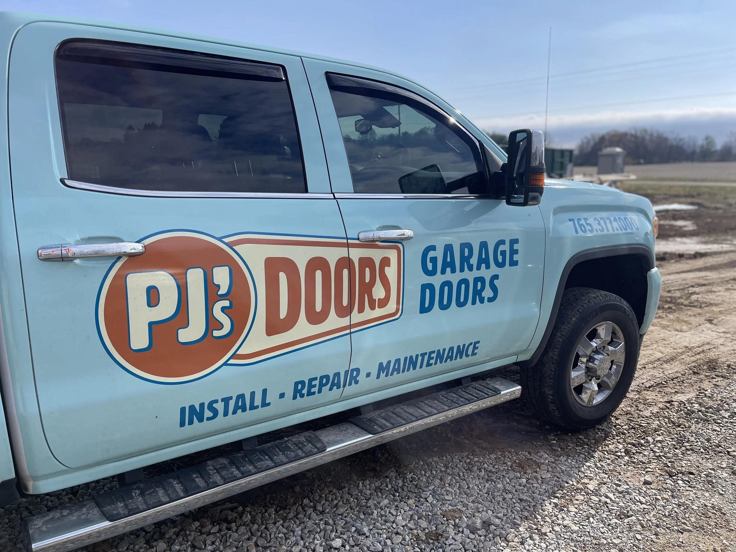 Two smiling men taking a selfie indoors, with a garage door in the background. One wears a black cap, and the other wears a gray cap with a 'New Horizons' logo.