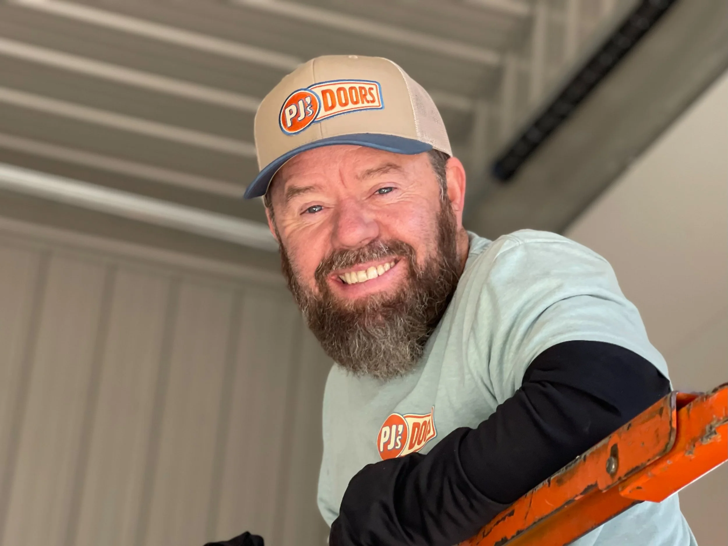 A man working on installing a white garage door in a garage construction site, with an open garage space and wooden framing inside.