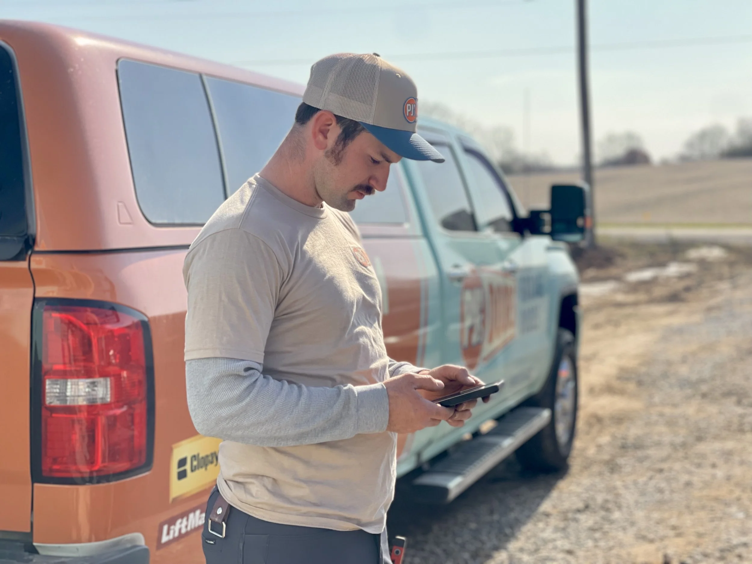 Two smiling men taking a selfie indoors, with a garage door in the background. One wears a black cap, and the other wears a gray cap with a 'New Horizons' logo.