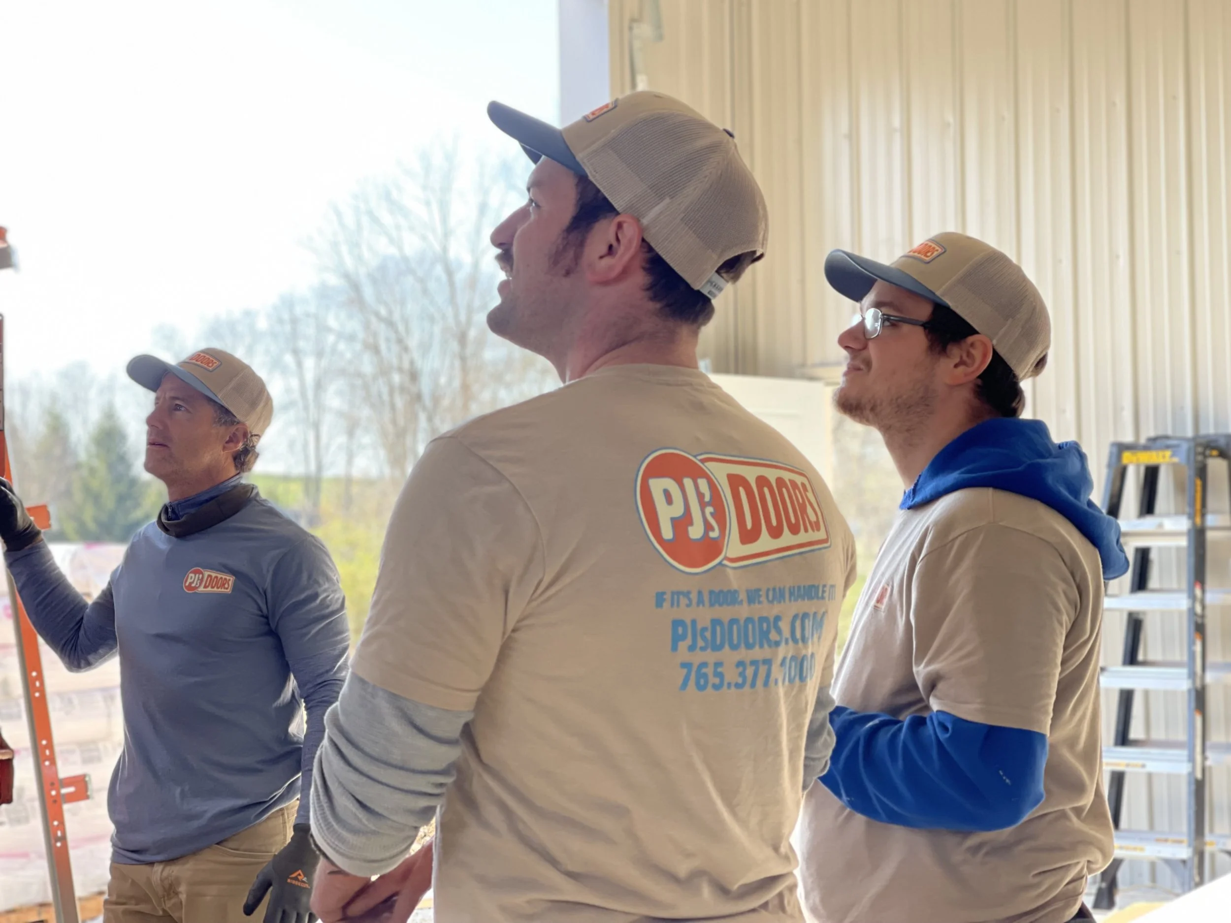 A man working on installing a white garage door in a garage construction site, with an open garage space and wooden framing inside.