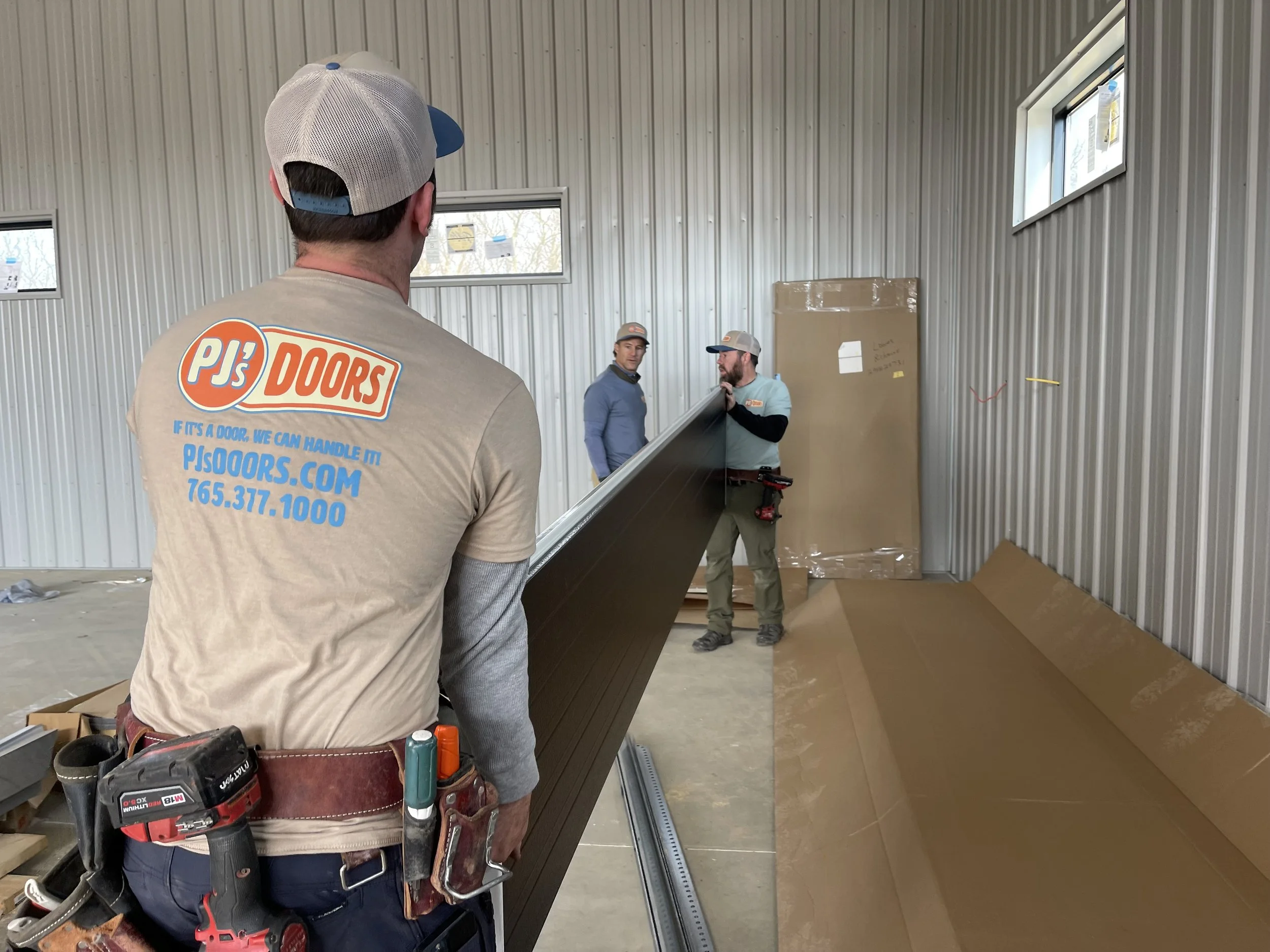 Three workers installing a metal door frame inside a building with unfinished walls and small windows.