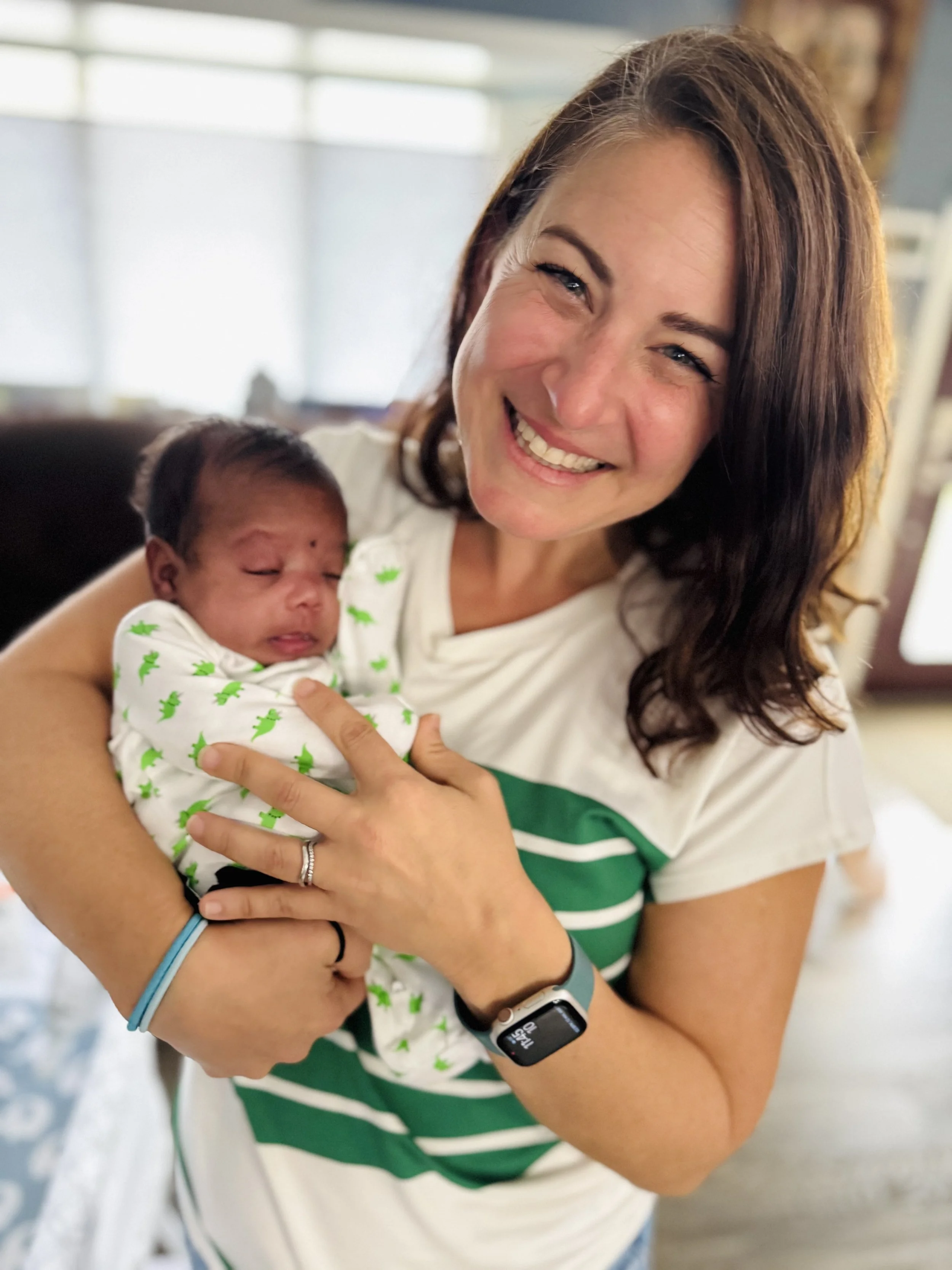 A woman holding a newborn baby indoors, smiling at the camera.