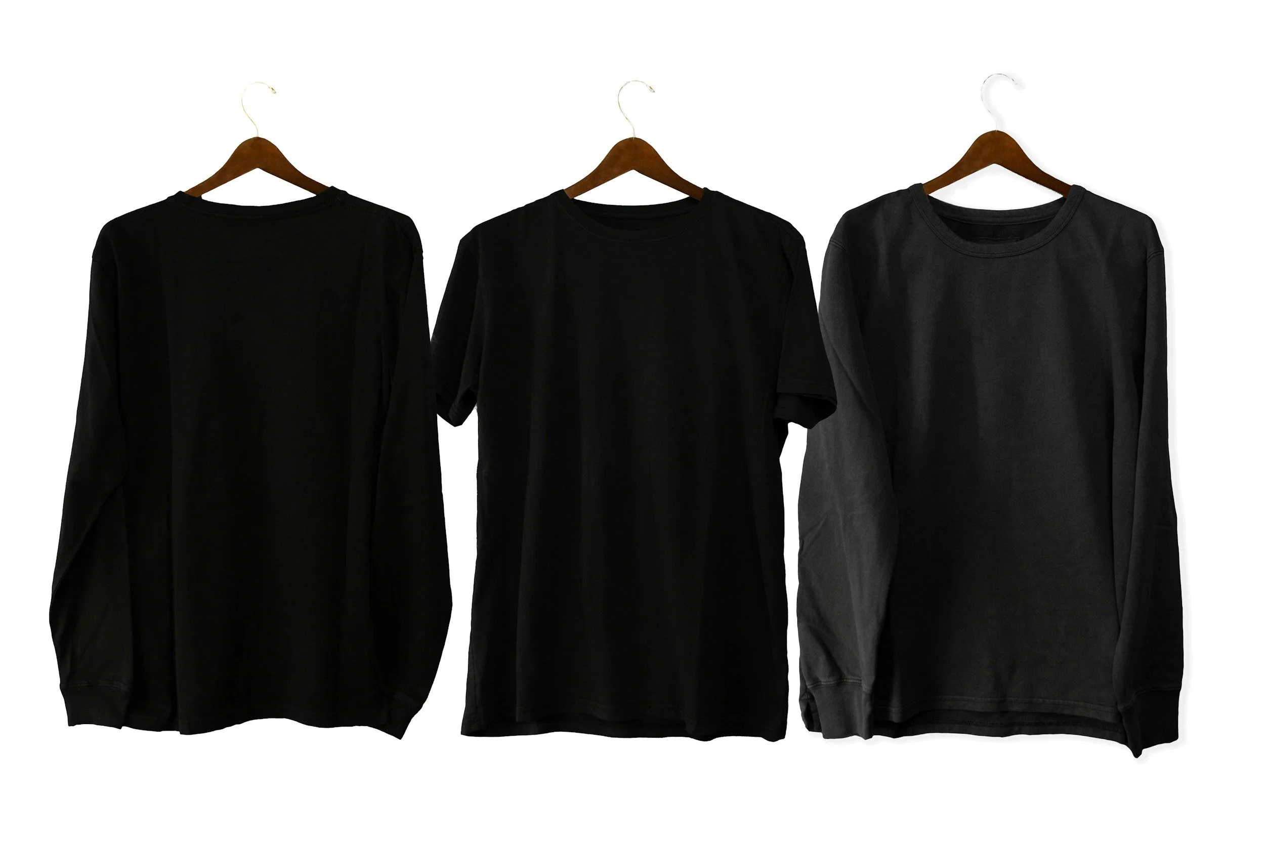 Three black clothing items hanging on wooden hangers against a white background; a long-sleeve shirt on the left, a short-sleeve shirt in the middle, and a sweatshirt on the right.