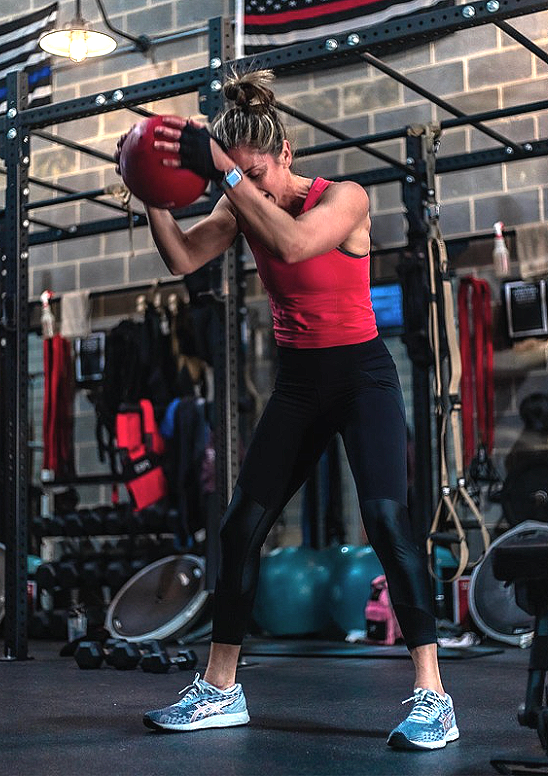 A woman in athletic attire performing a workout with a medicine ball in a gym.