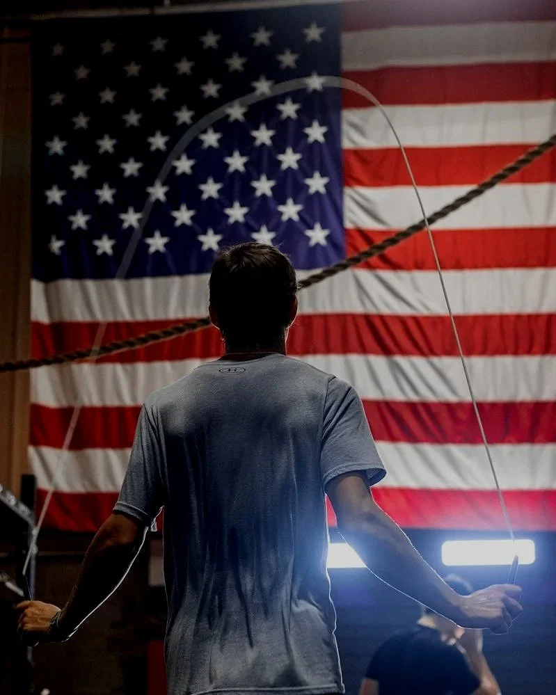 A person holding a jump rope in front of a large American flag.