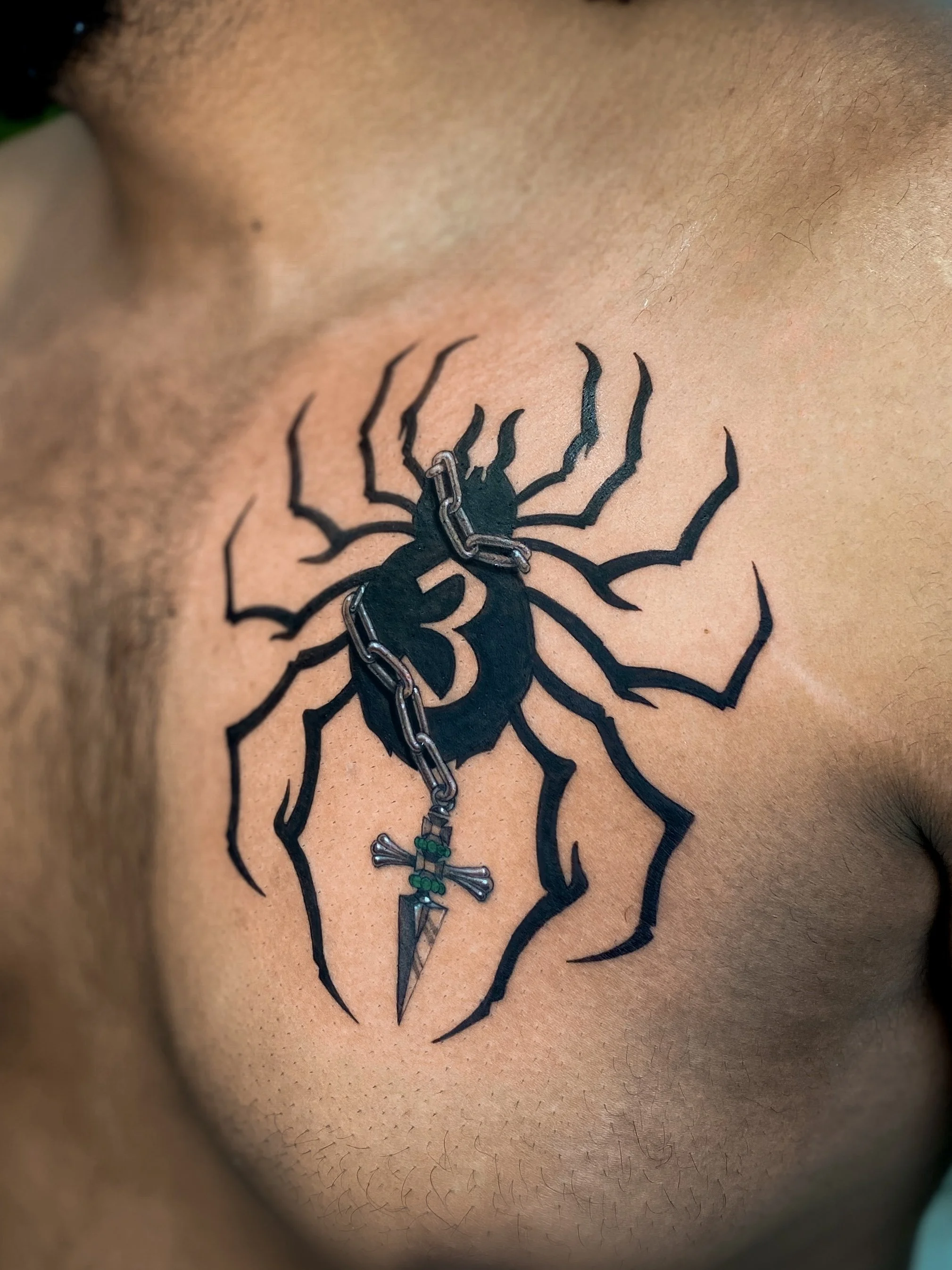 Tattoo of a black spider with a dagger in its body, on a person's chest.