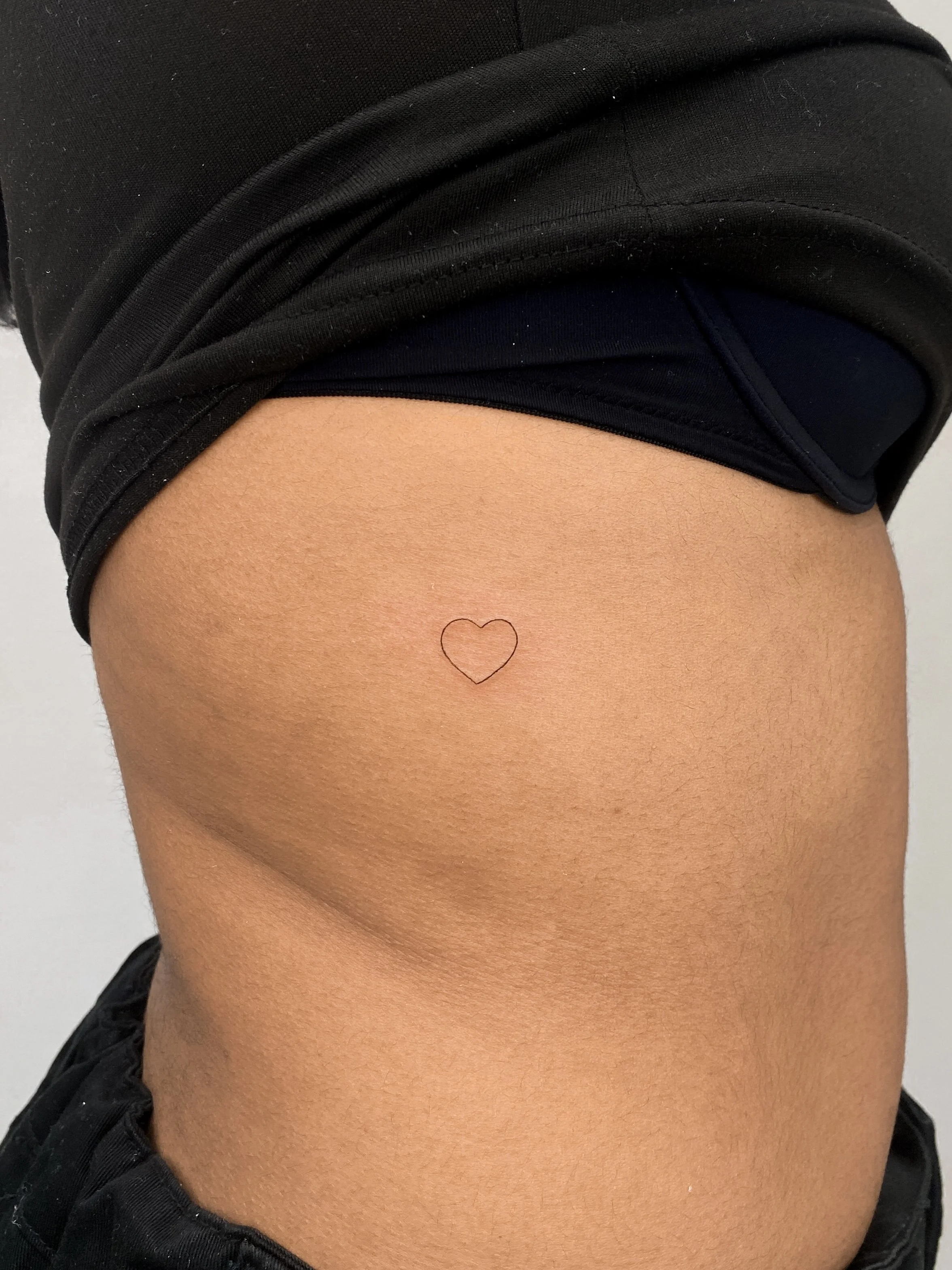 Close-up of a person's side torso, showing a small heart-shaped tattoo near the ribcage.