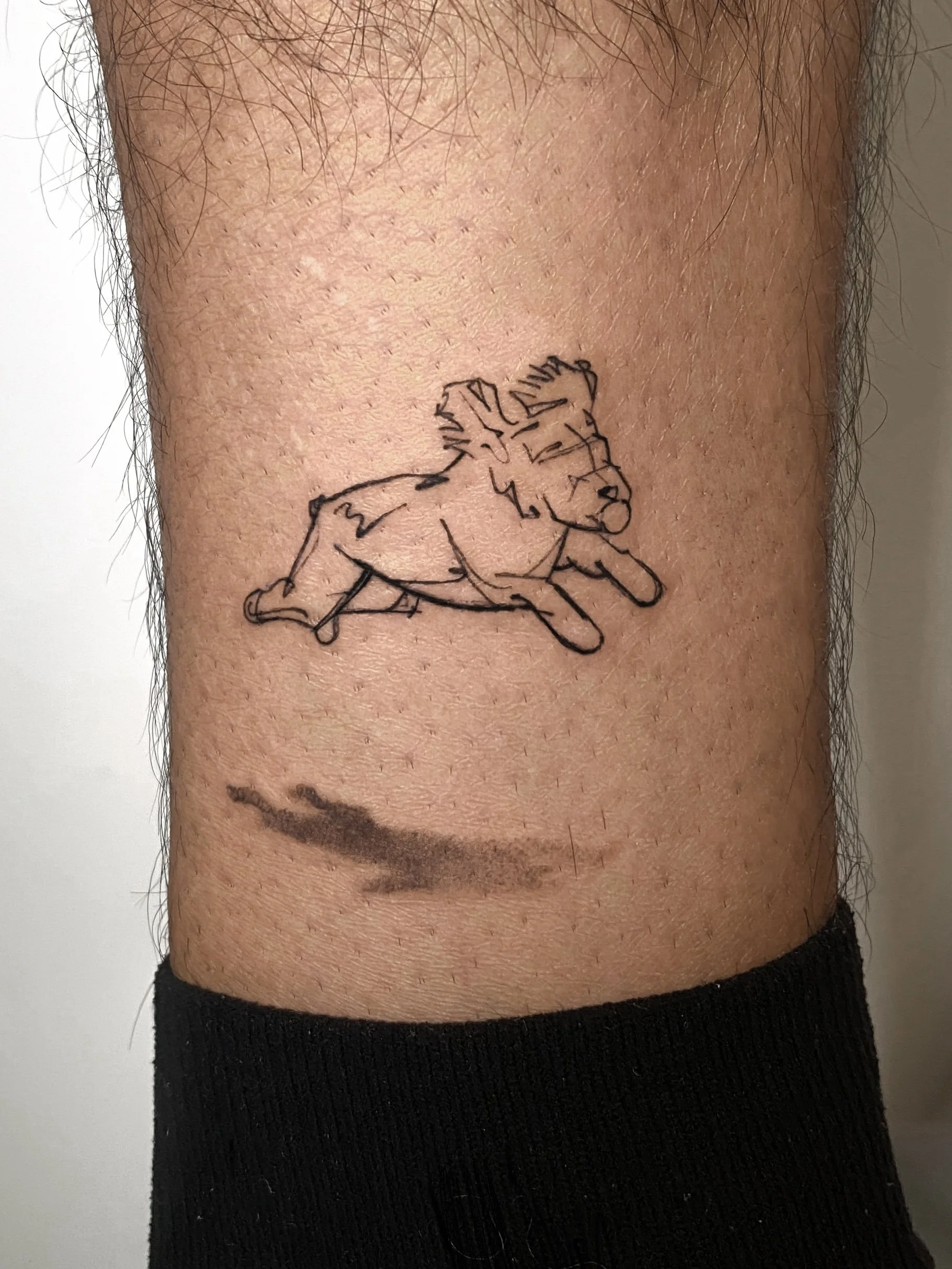 Tattoo of a running cartoon-style animal, possibly a bear or dog, on a person's leg.
