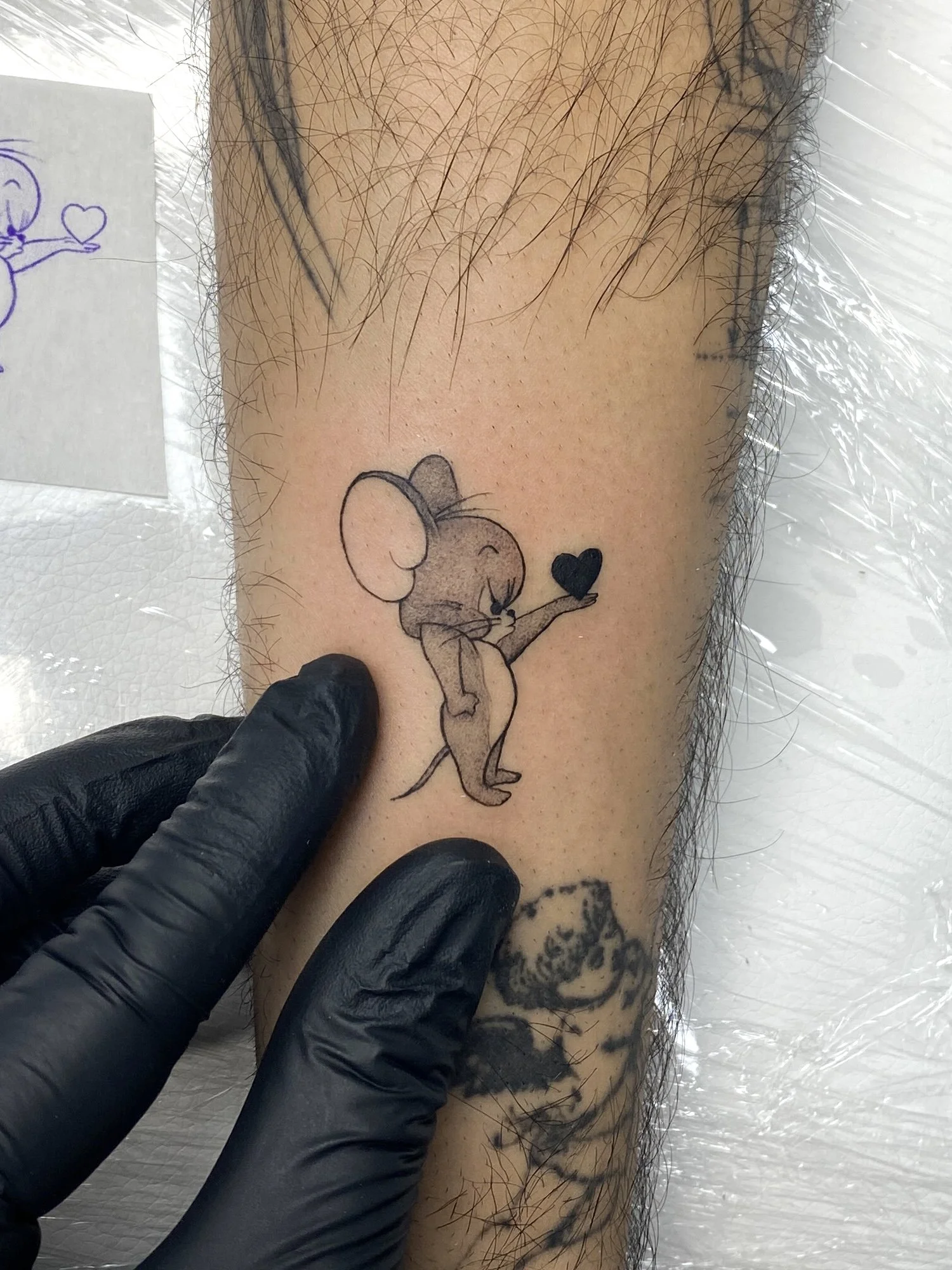Tattoo of a cartoon mouse holding a small black heart.