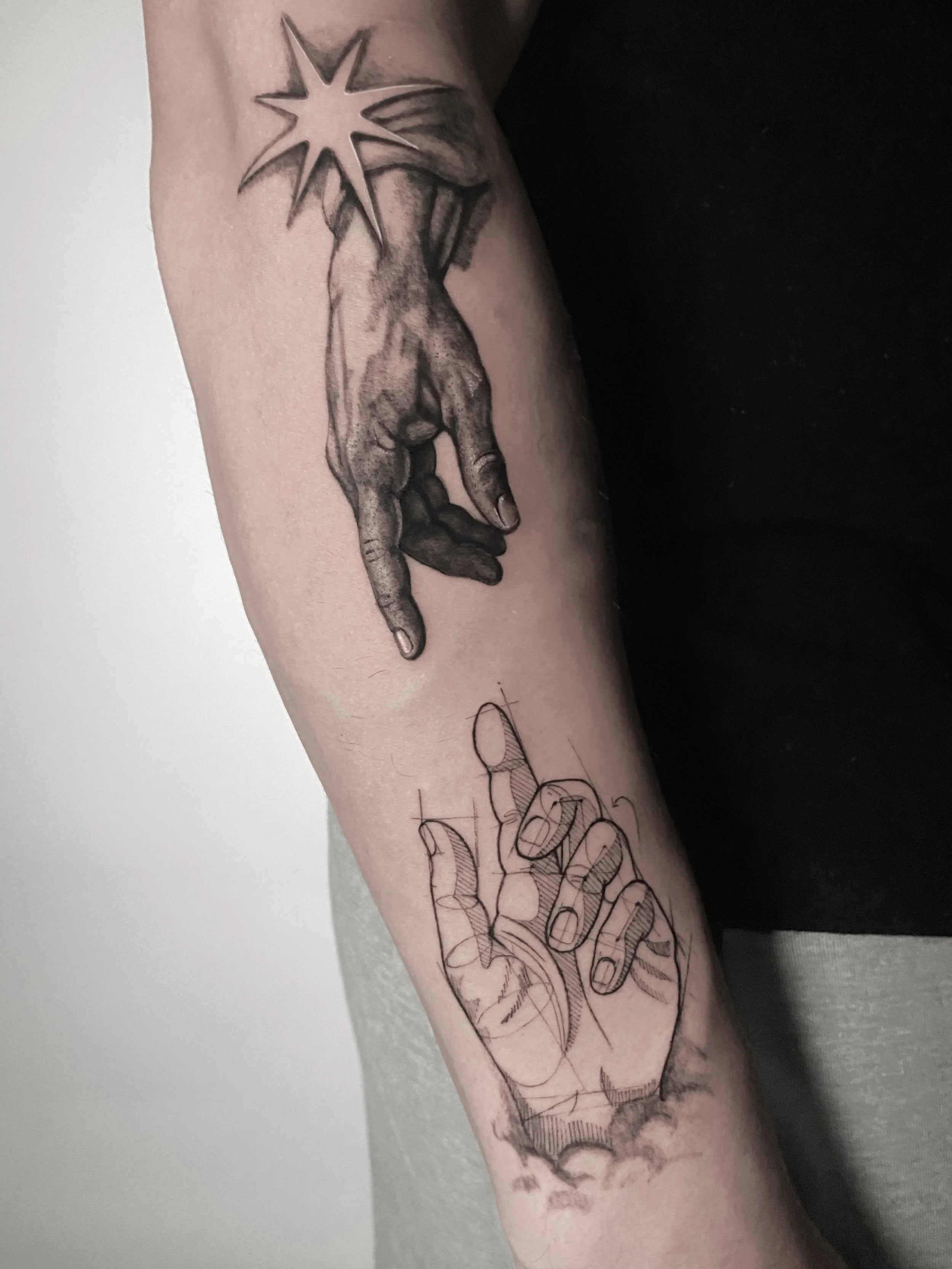 Tattoo of a realistic hand pointing downward, completed in black ink, with an outline sketch of the same hand below, on a person's forearm.