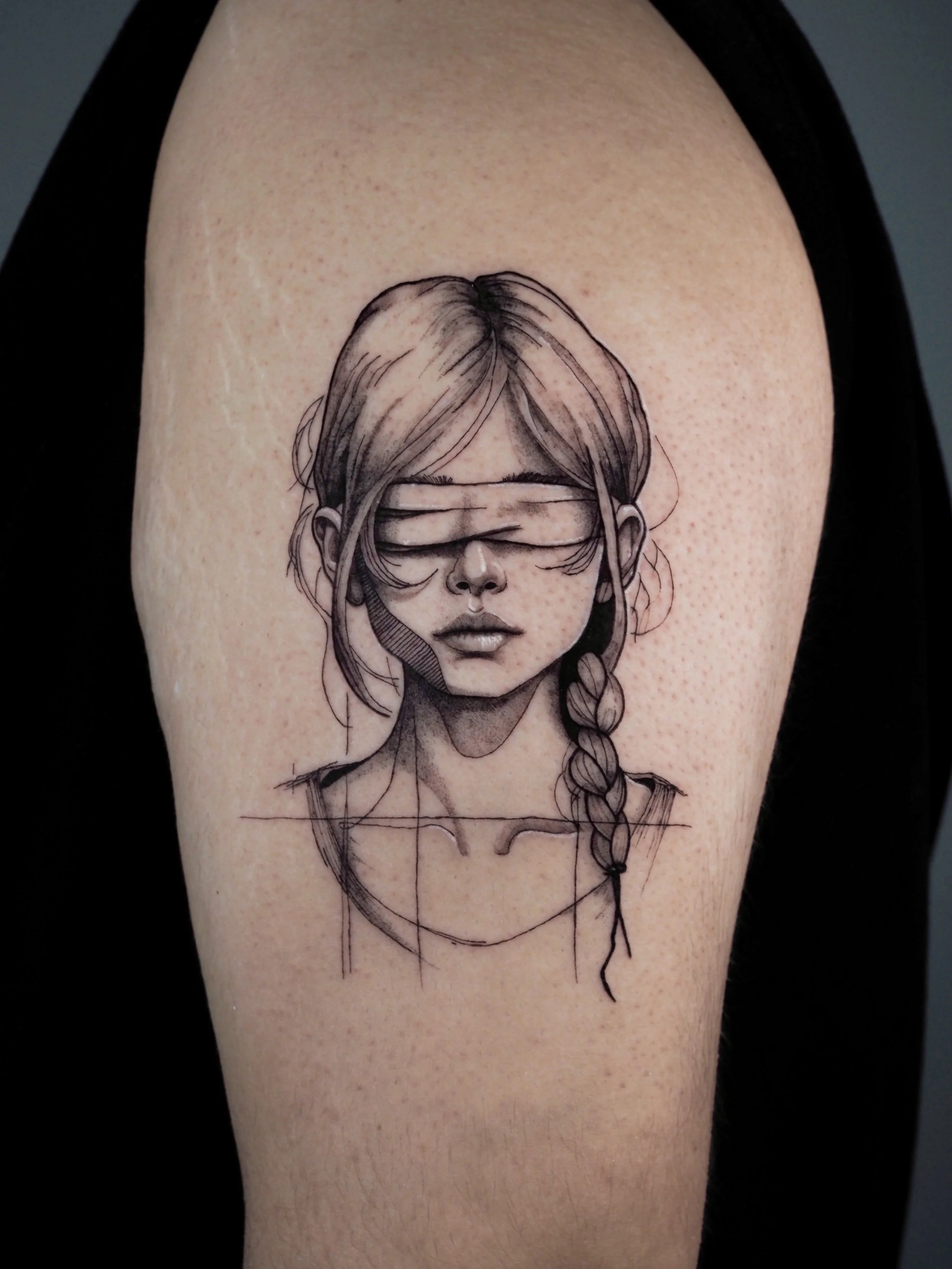 Black and gray tattoo of a woman with her eyes covered by a blindfold, styled in a sketch-like art on upper arm