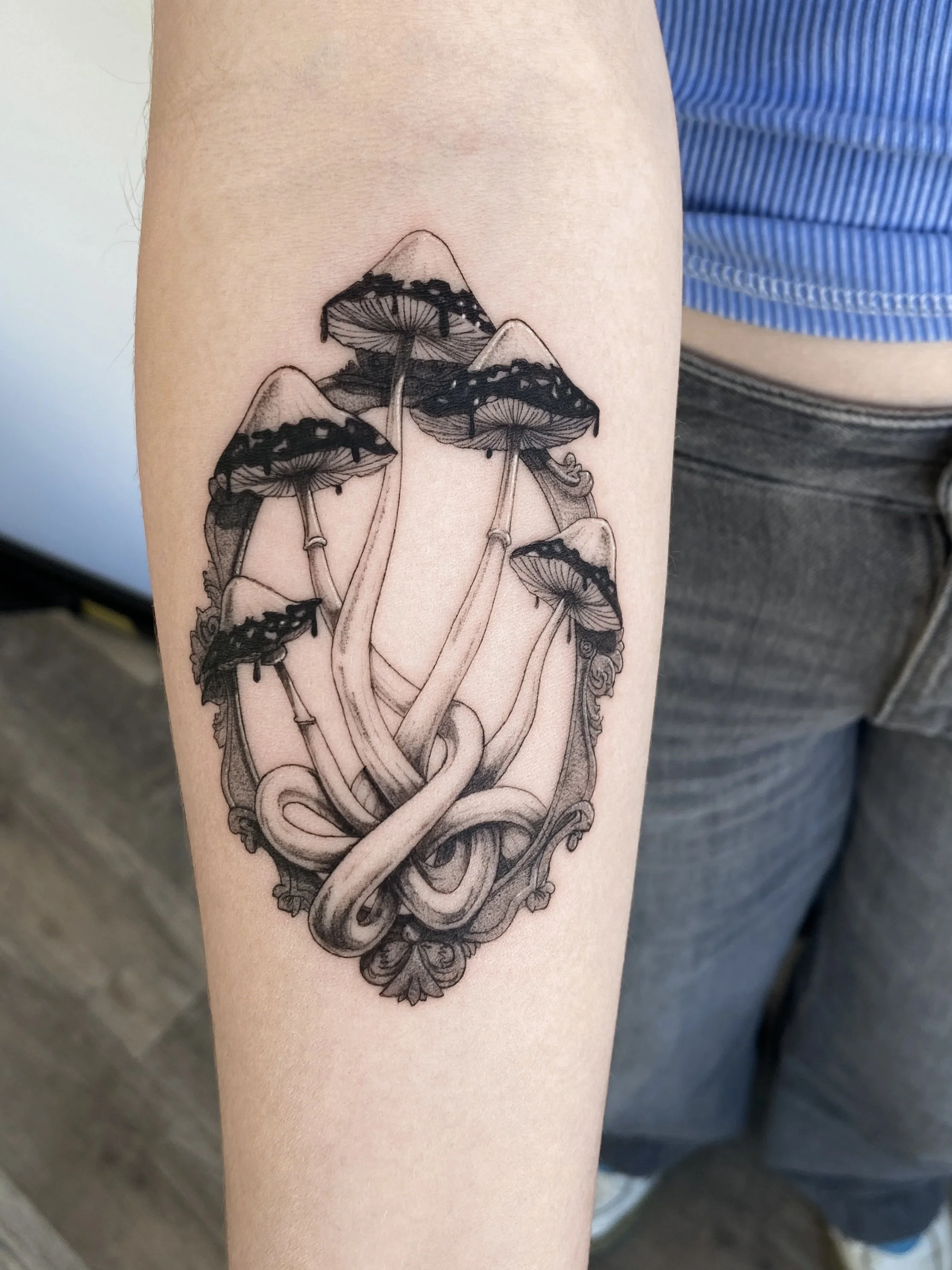 Black and gray tattoo of mushrooms and a snake intertwining on the person's arm.