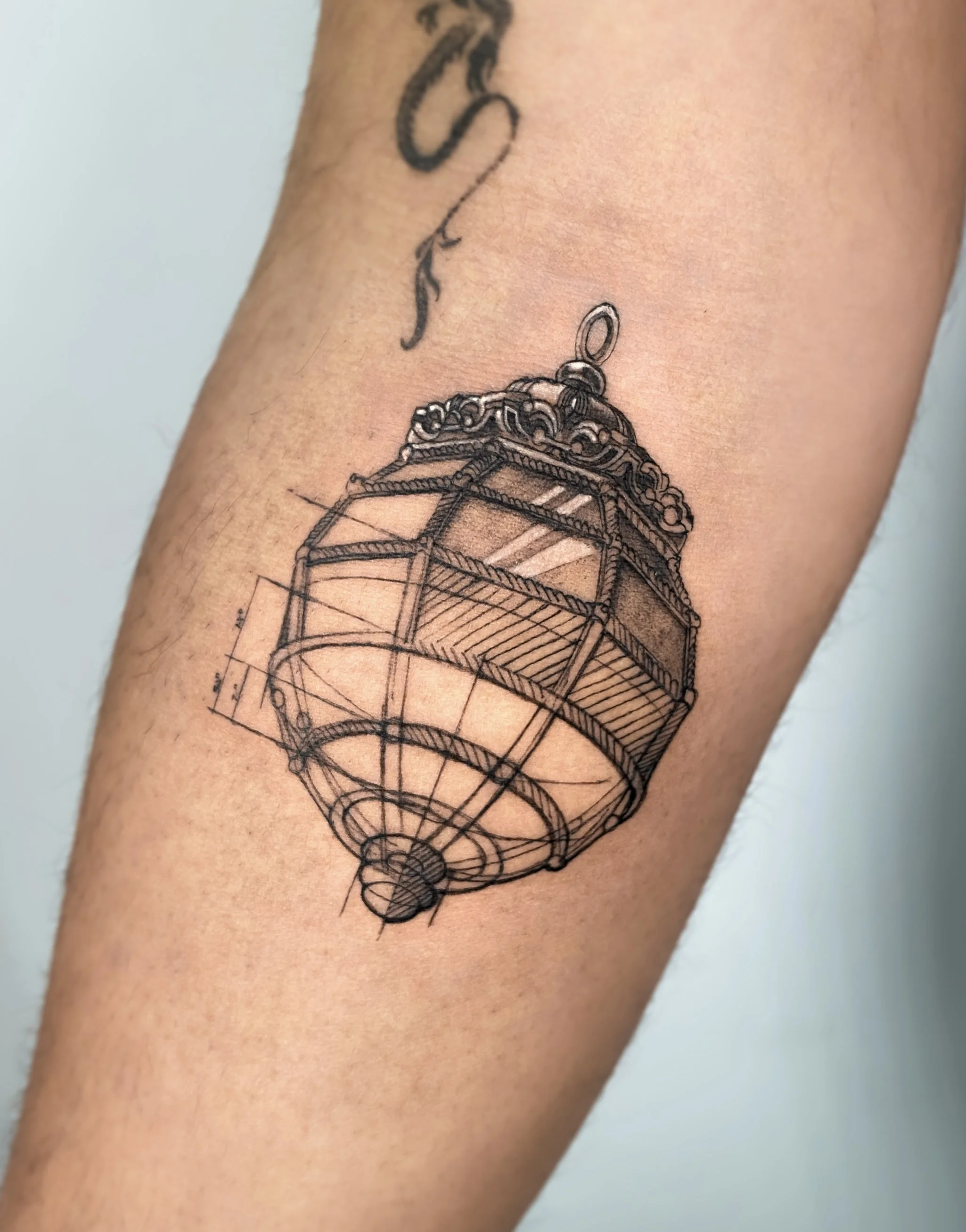 Tattoo of a detailed lantern in black ink on skin, with blueprint-style lines and measurements.