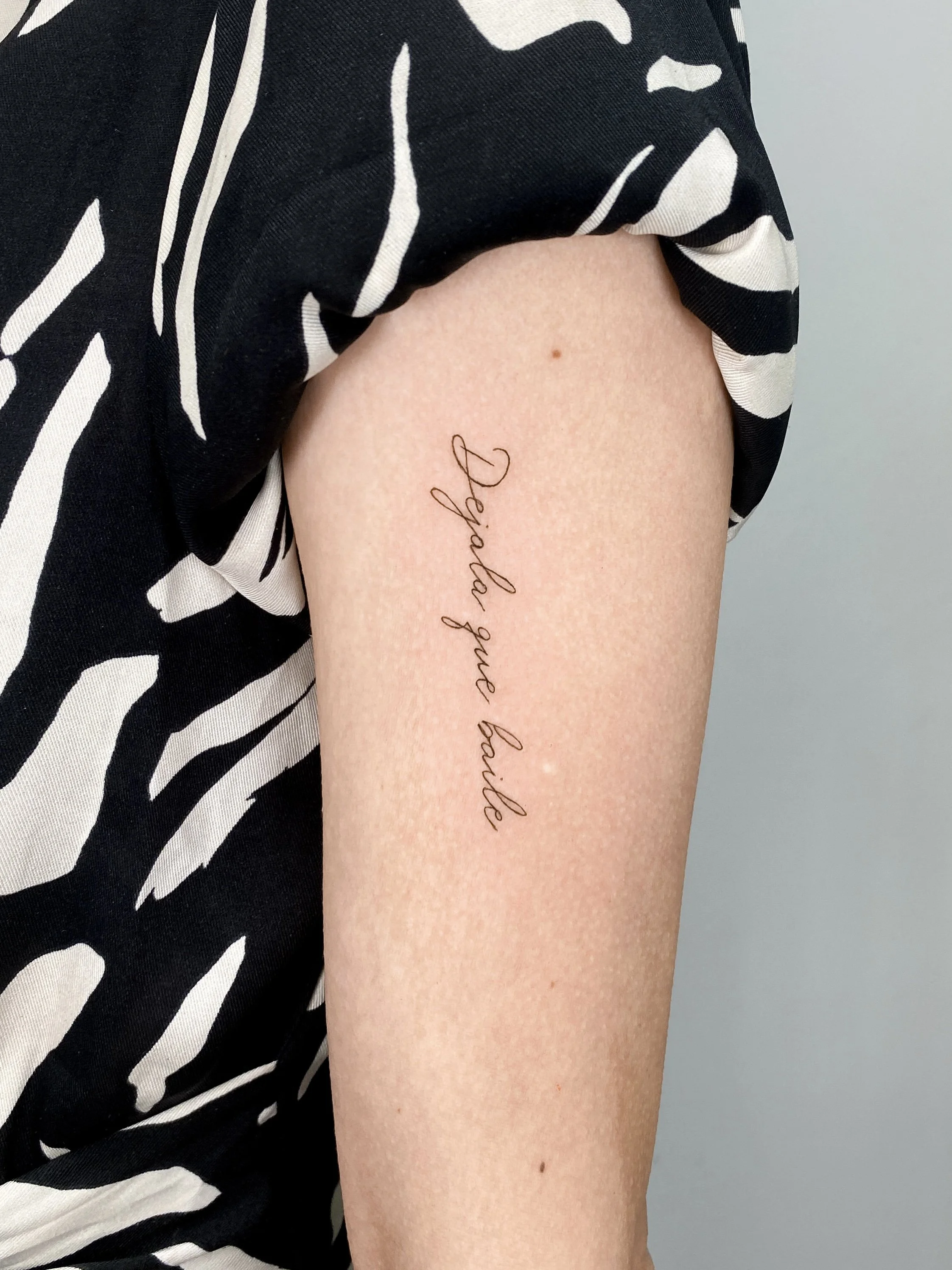 A close-up of a person's upper arm with a tattoo that reads 'Dig in and love' in cursive script, next to a black and white patterned shirt.