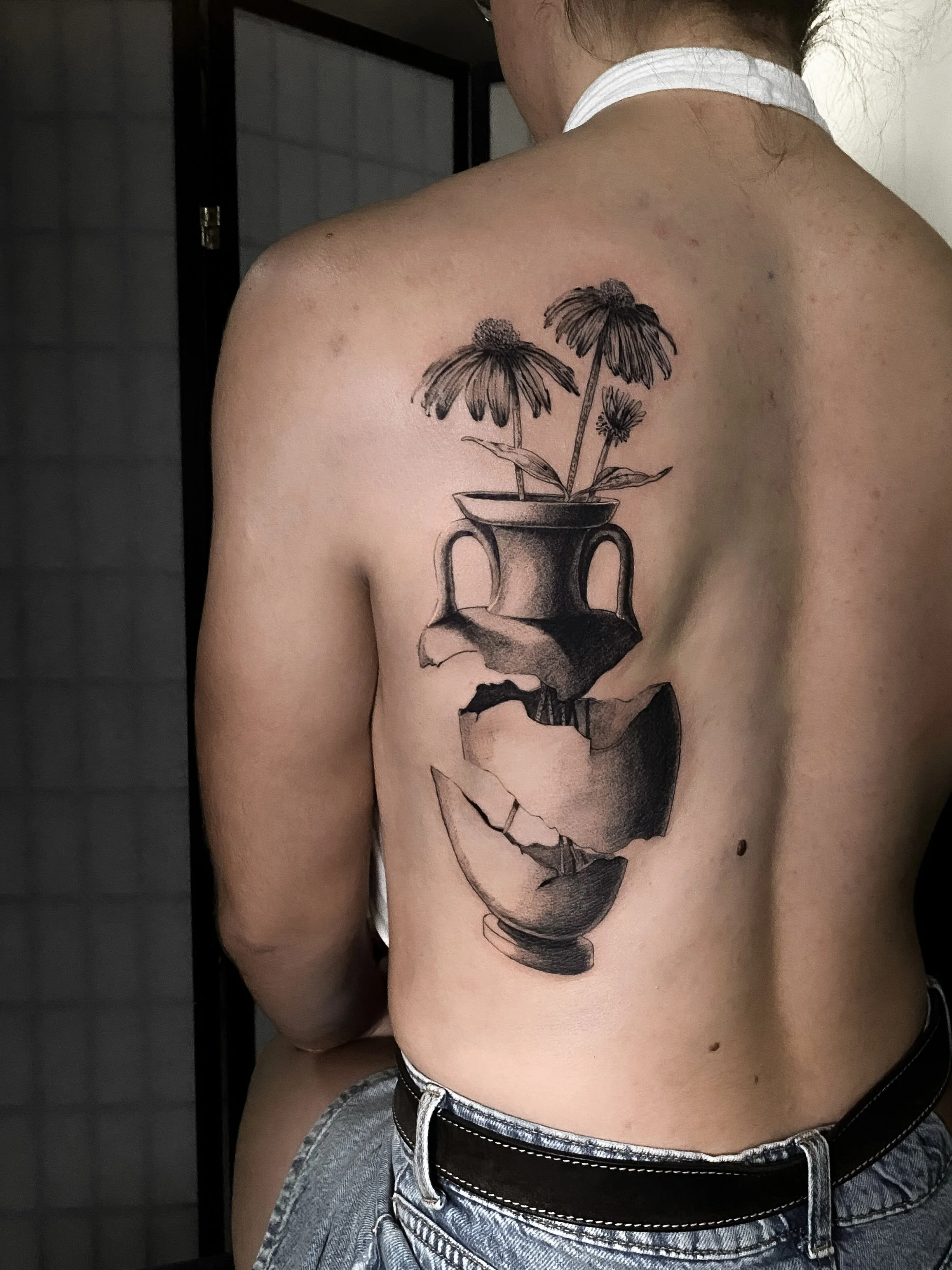 Tattoo of a broken vase with flowers on a person's back.