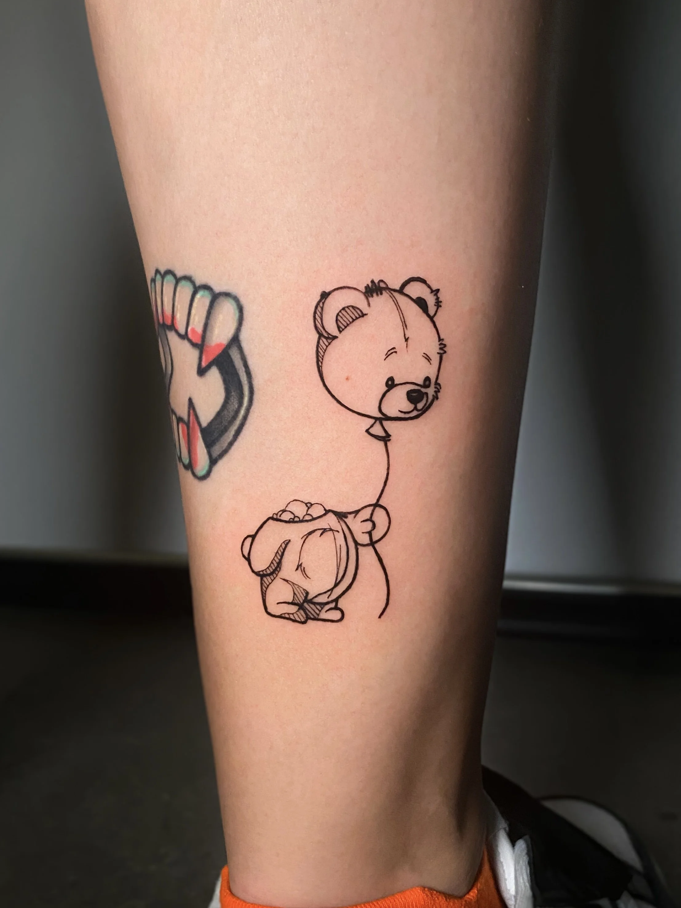 Tattoo of a cartoon bear holding a balloon and a small animal, possibly a dog, on the person's lower leg.