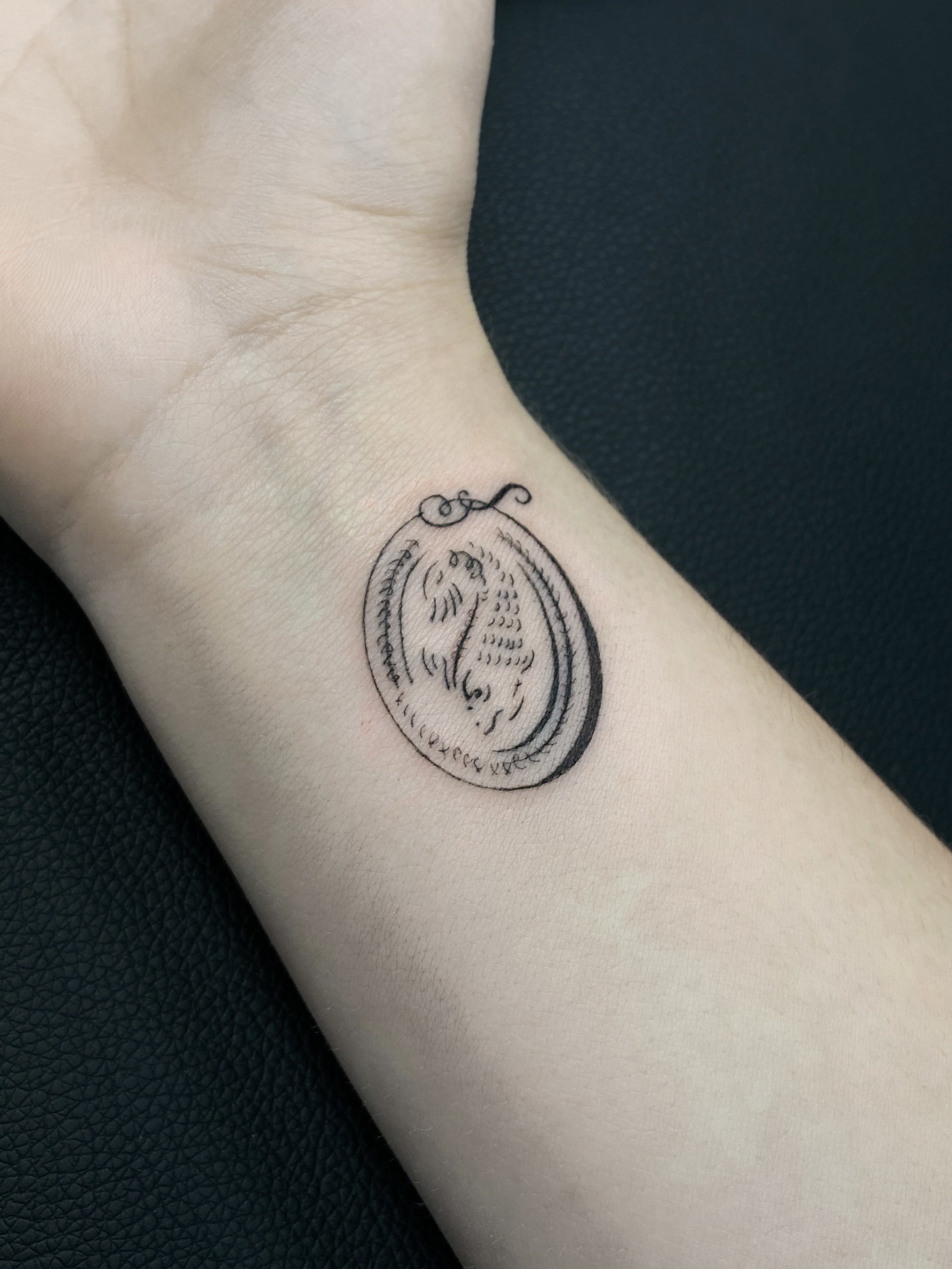 Tattoo of a pocket watch on a person's wrist, depicted with thin black lines.