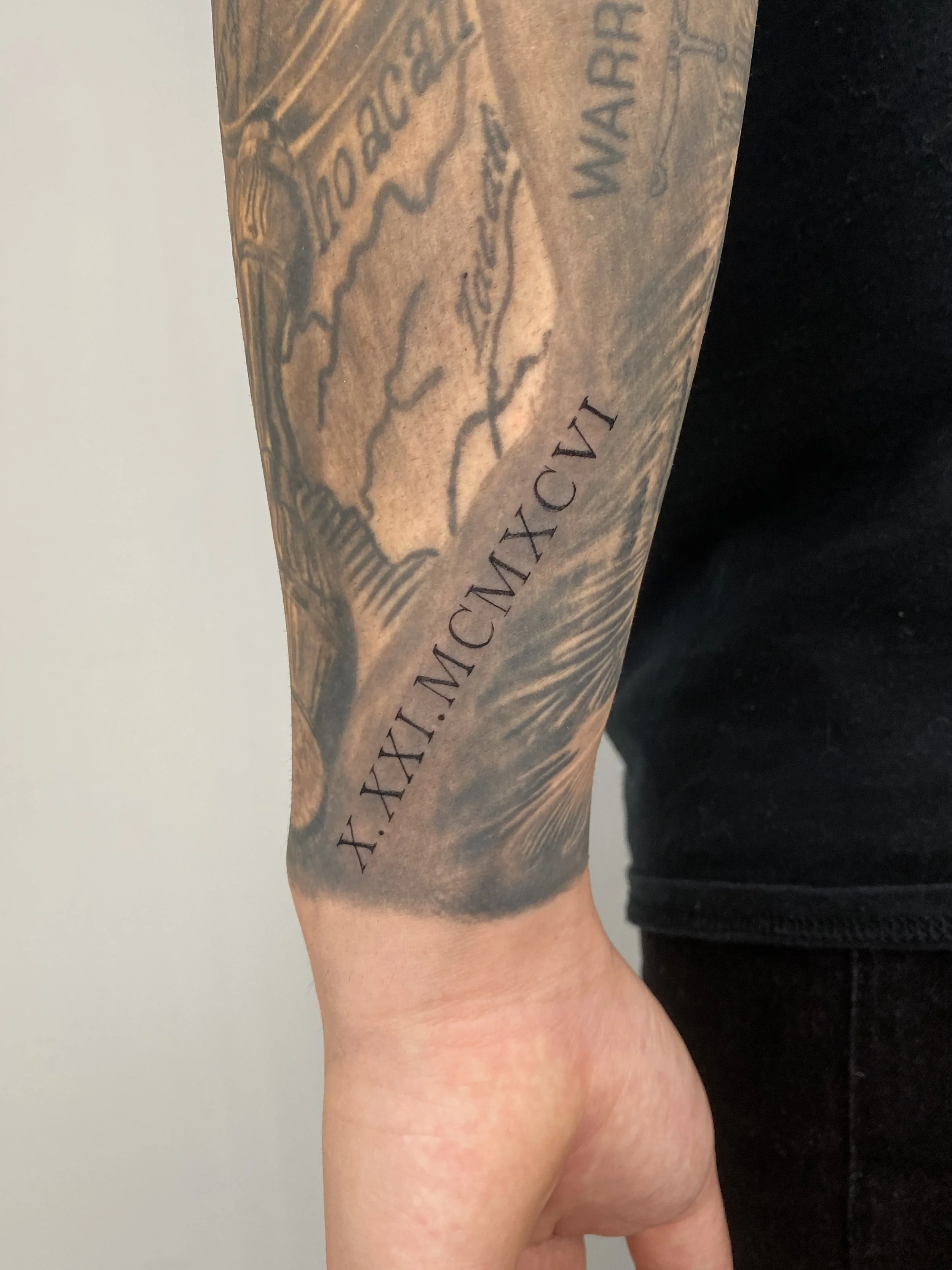 Close-up of a person's inner forearm with a tattoo of a map and the Latin phrase 'XXIX MCMXCV'.