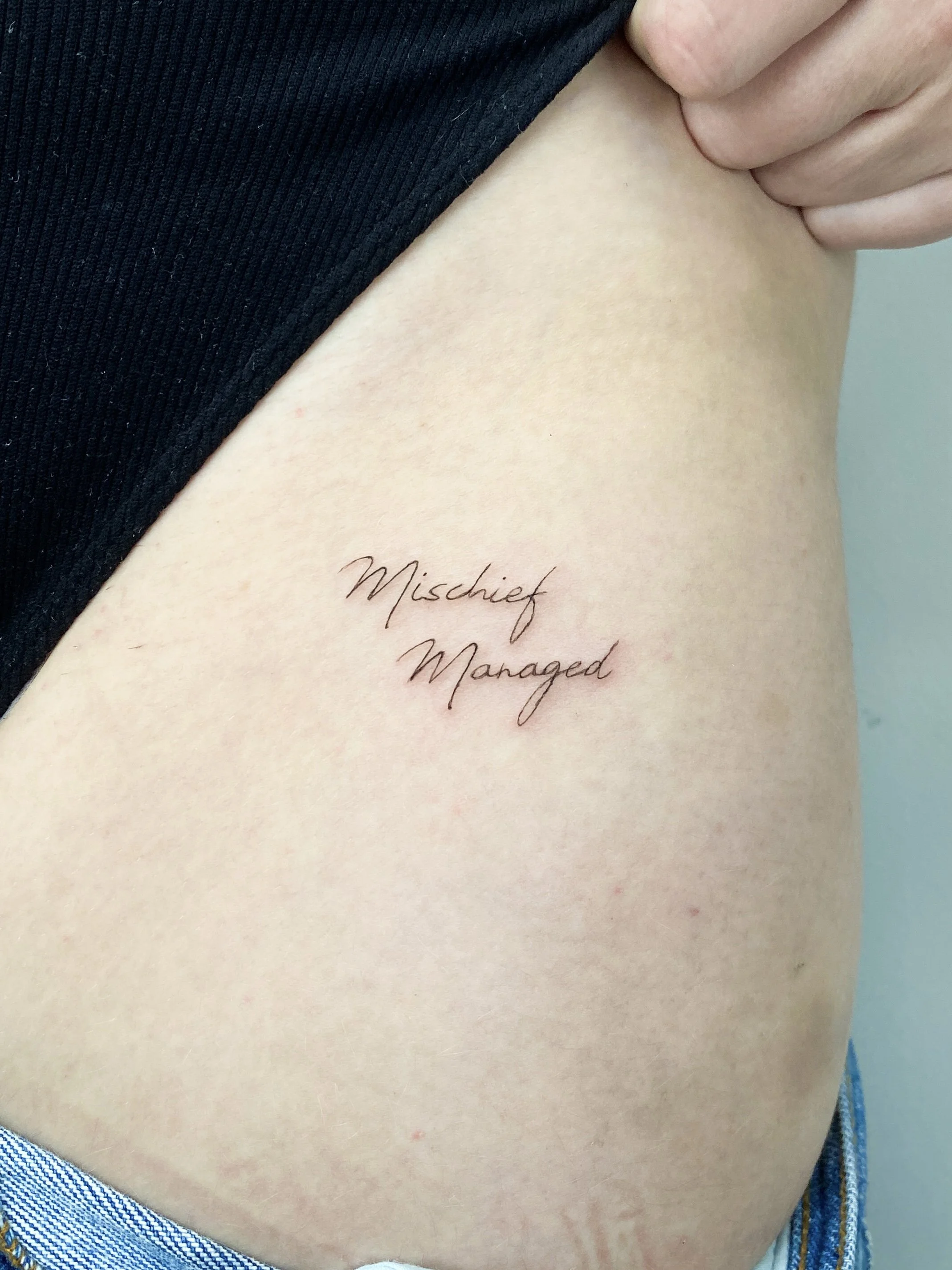 Tattoo on person's side reading 'Mischief Managed' in cursive.
