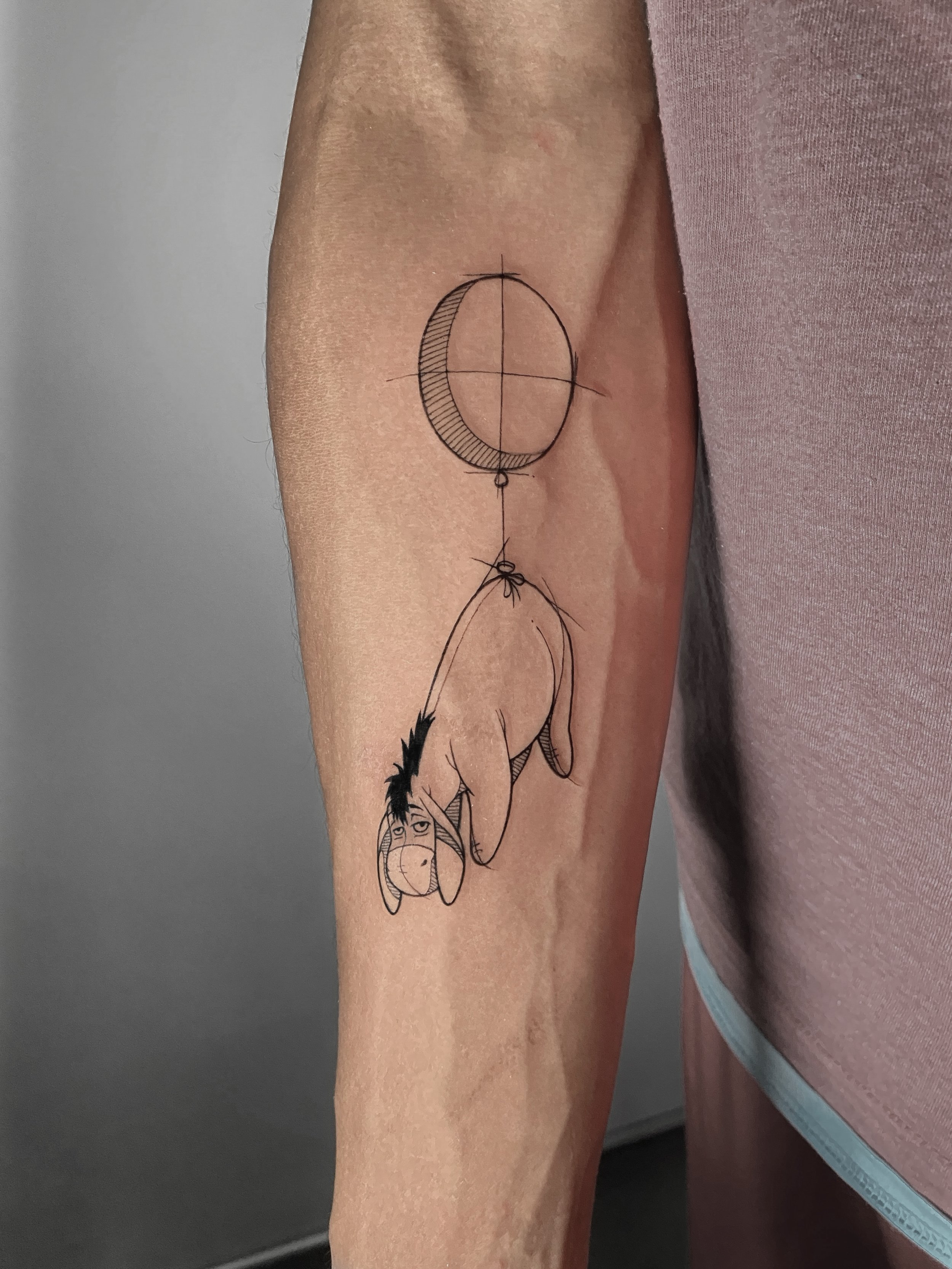 Tattoo of Eeyore from Winnie the Pooh hanging from a balloon on a person's inner arm.