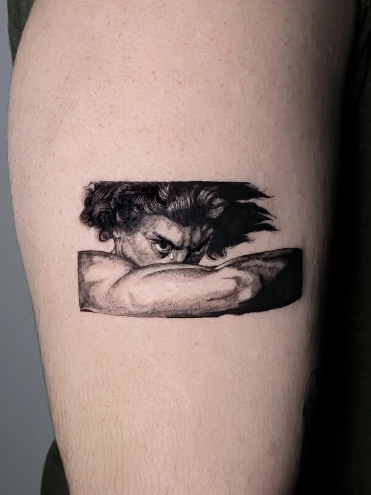 Black and gray tattoo of a woman with curly hair, resting her head on her arm, with an intense gaze, on a person's upper arm.