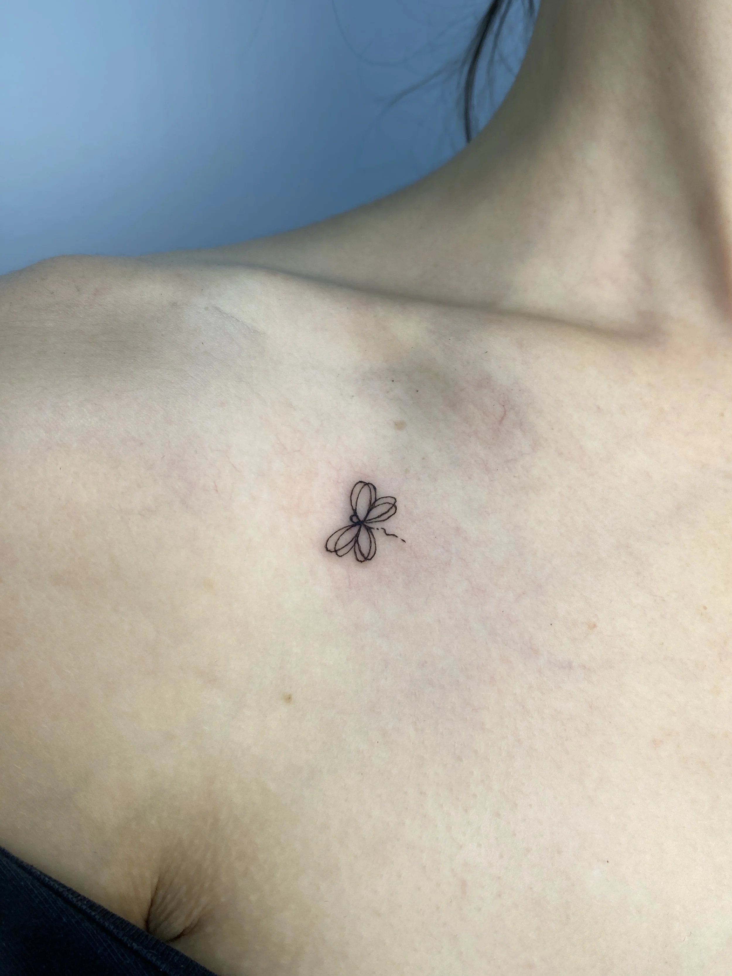 Close-up of a person's upper chest with a small tattoo of a butterfly on the skin.