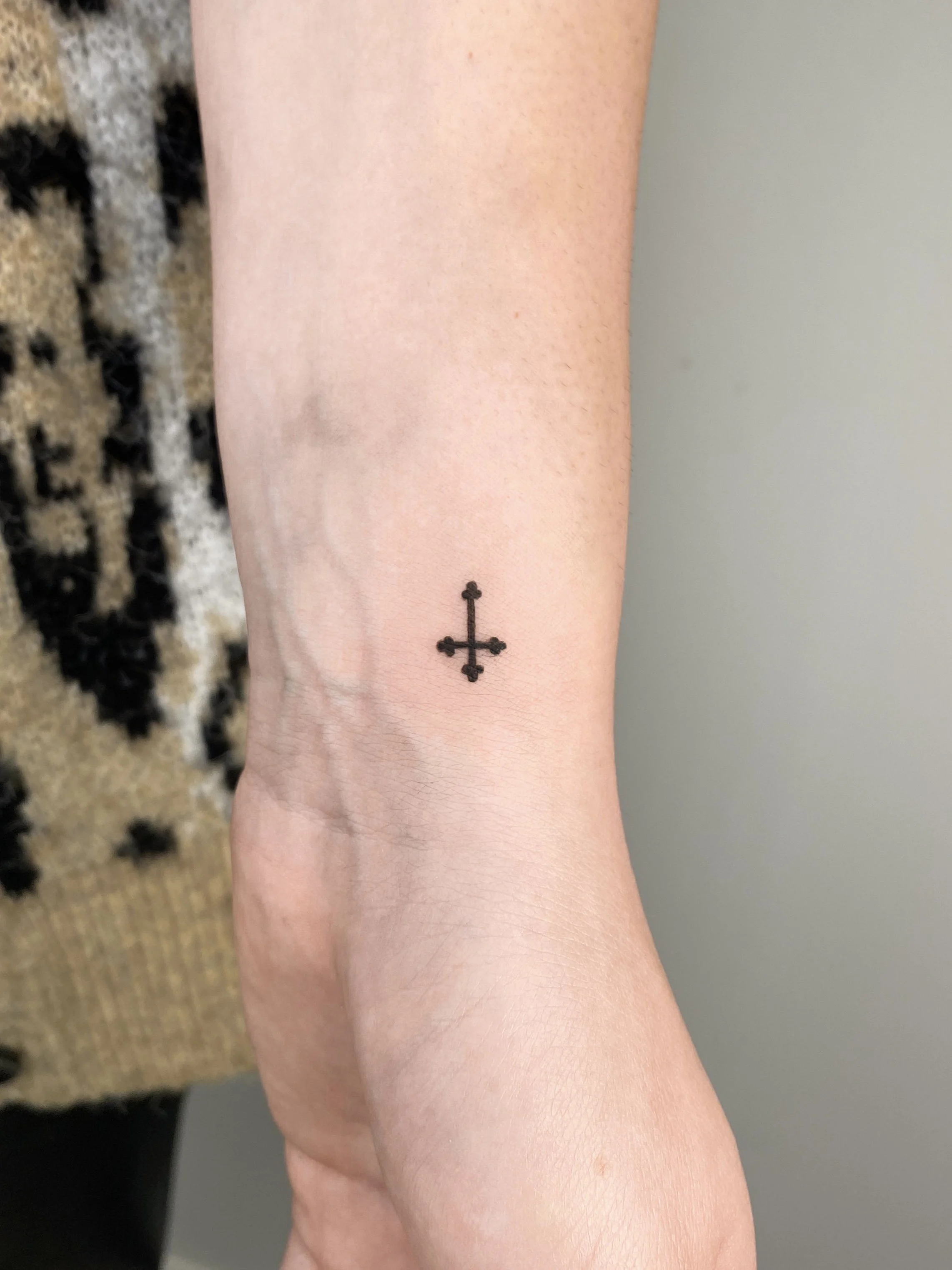 Small black cross tattoo on person's wrist.