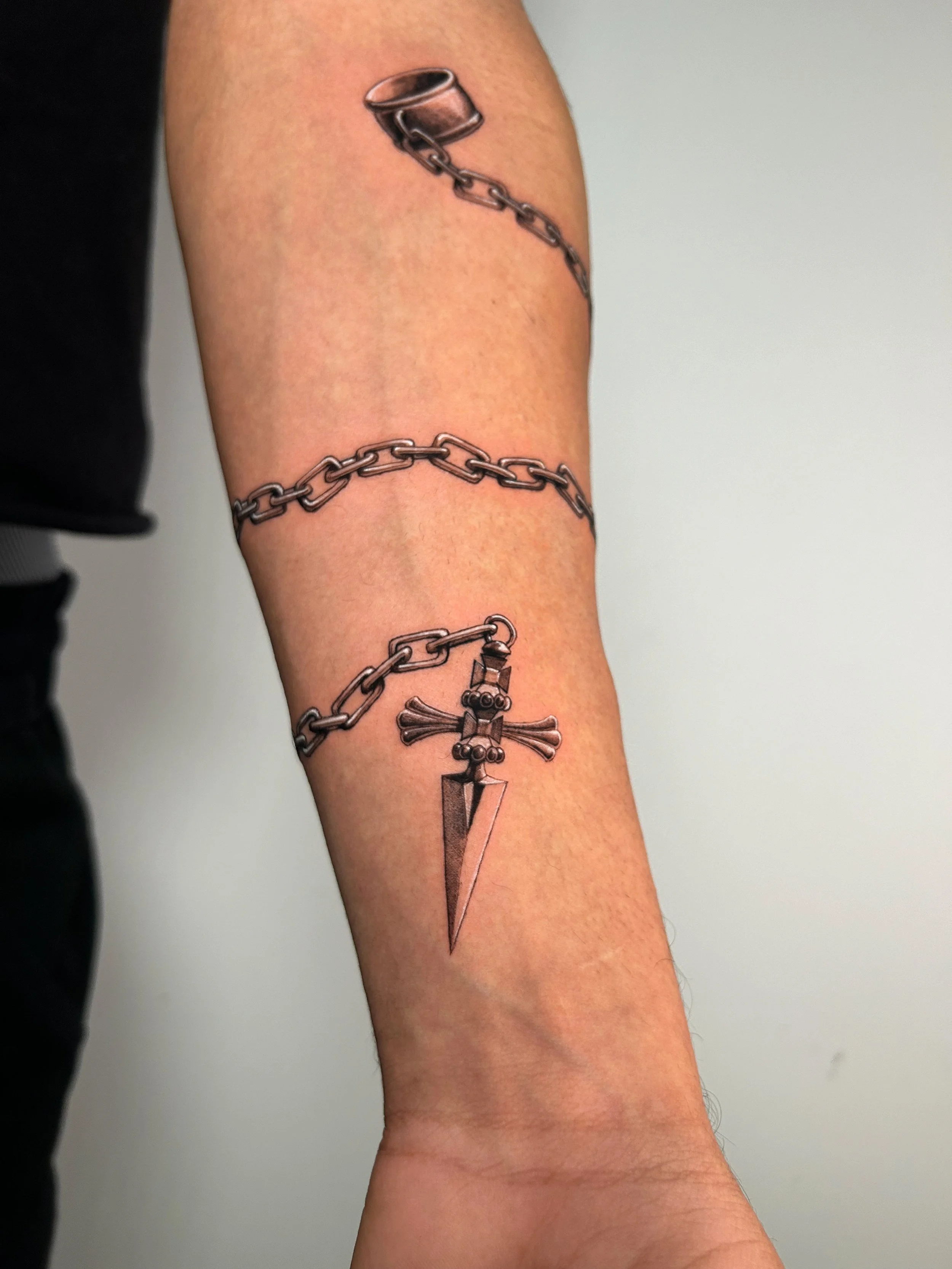 Tattoo of a chain and a dagger on a person's arm.