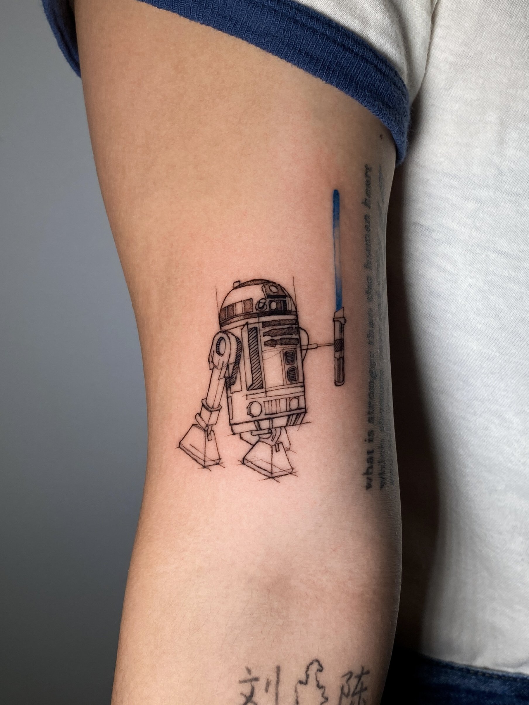 Tattoo of R2-D2 from Star Wars on a person's upper arm.