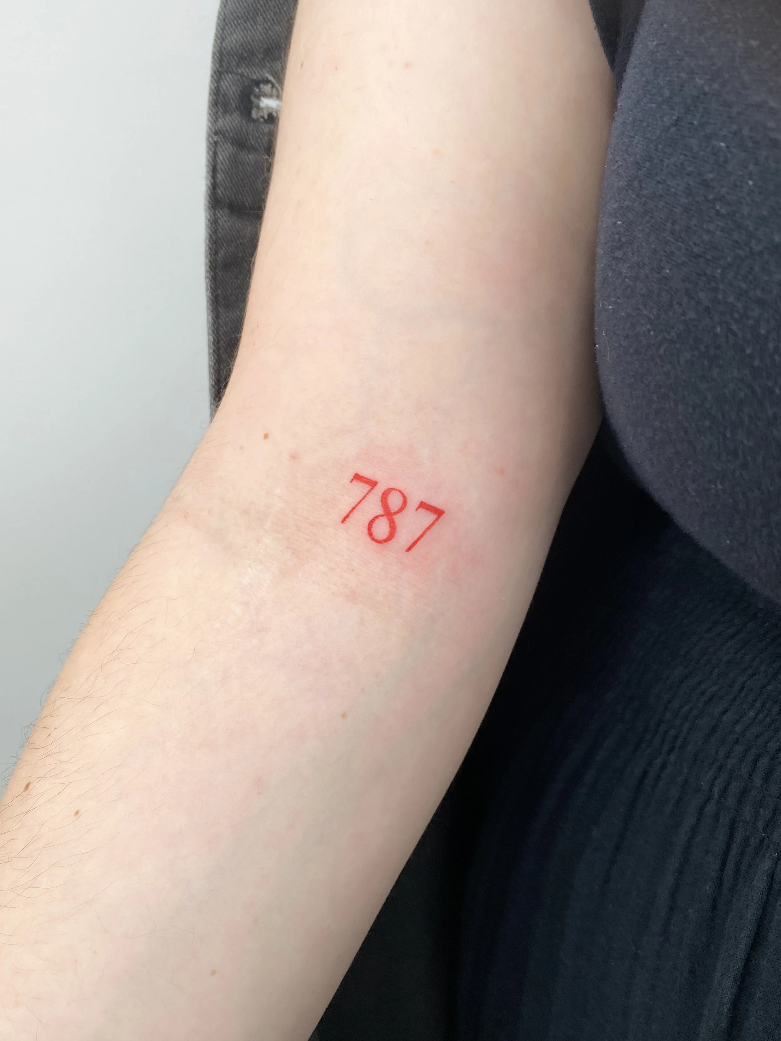 A person's forearm with a red tattoo of the number 787 on the inside of the arm.