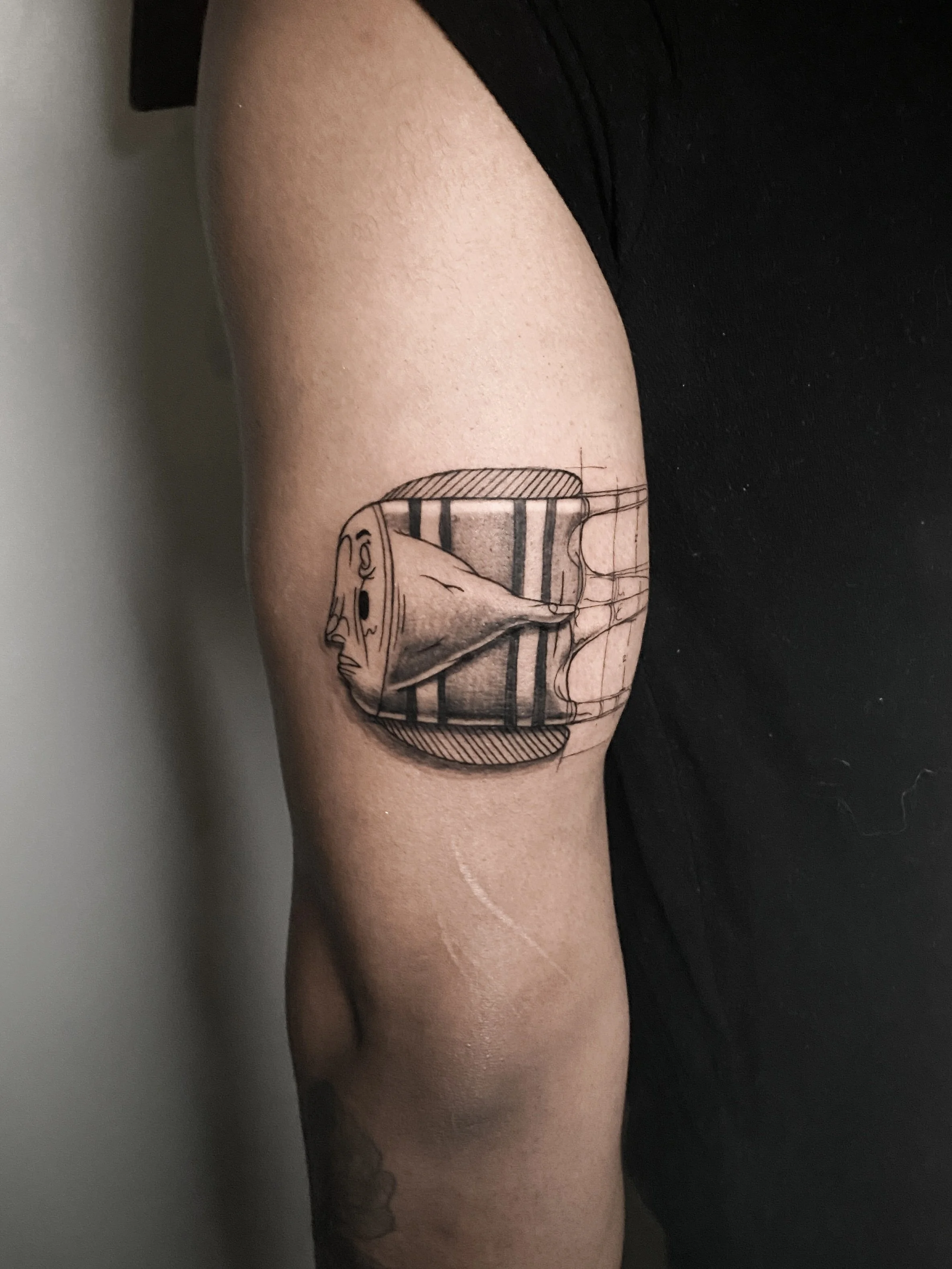A tattoo on a person's upper arm depicting a stylized human face, with bold black lines and shaded areas, integrated with geometric shapes and patterns.